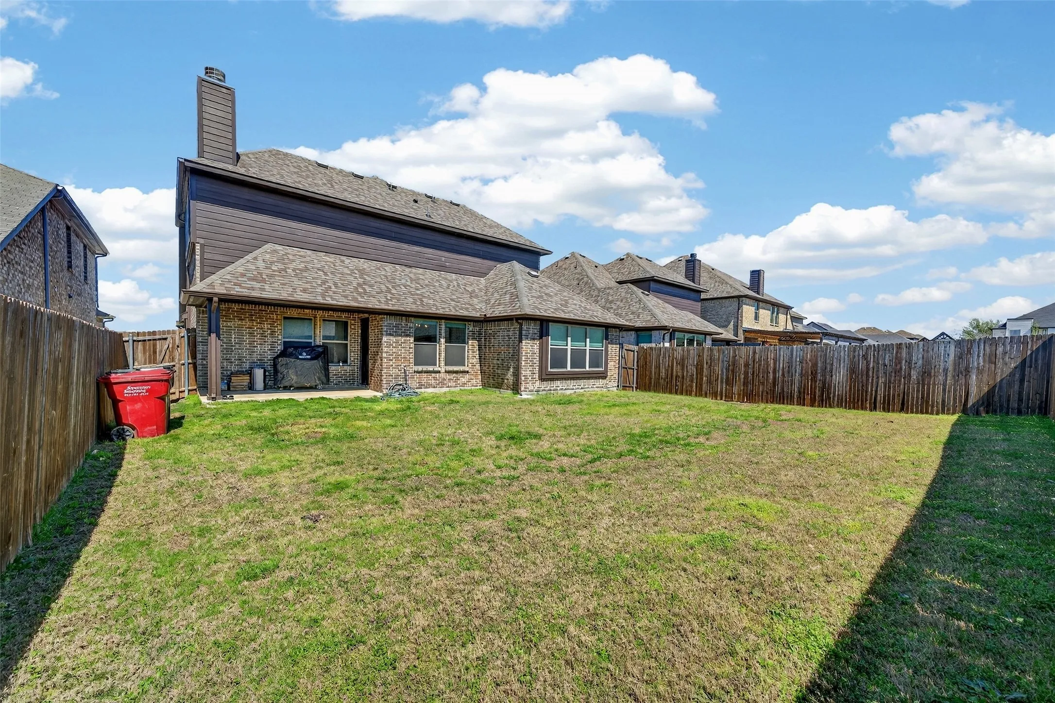 Expansive fenced backyard with a covered patio and brick exterior