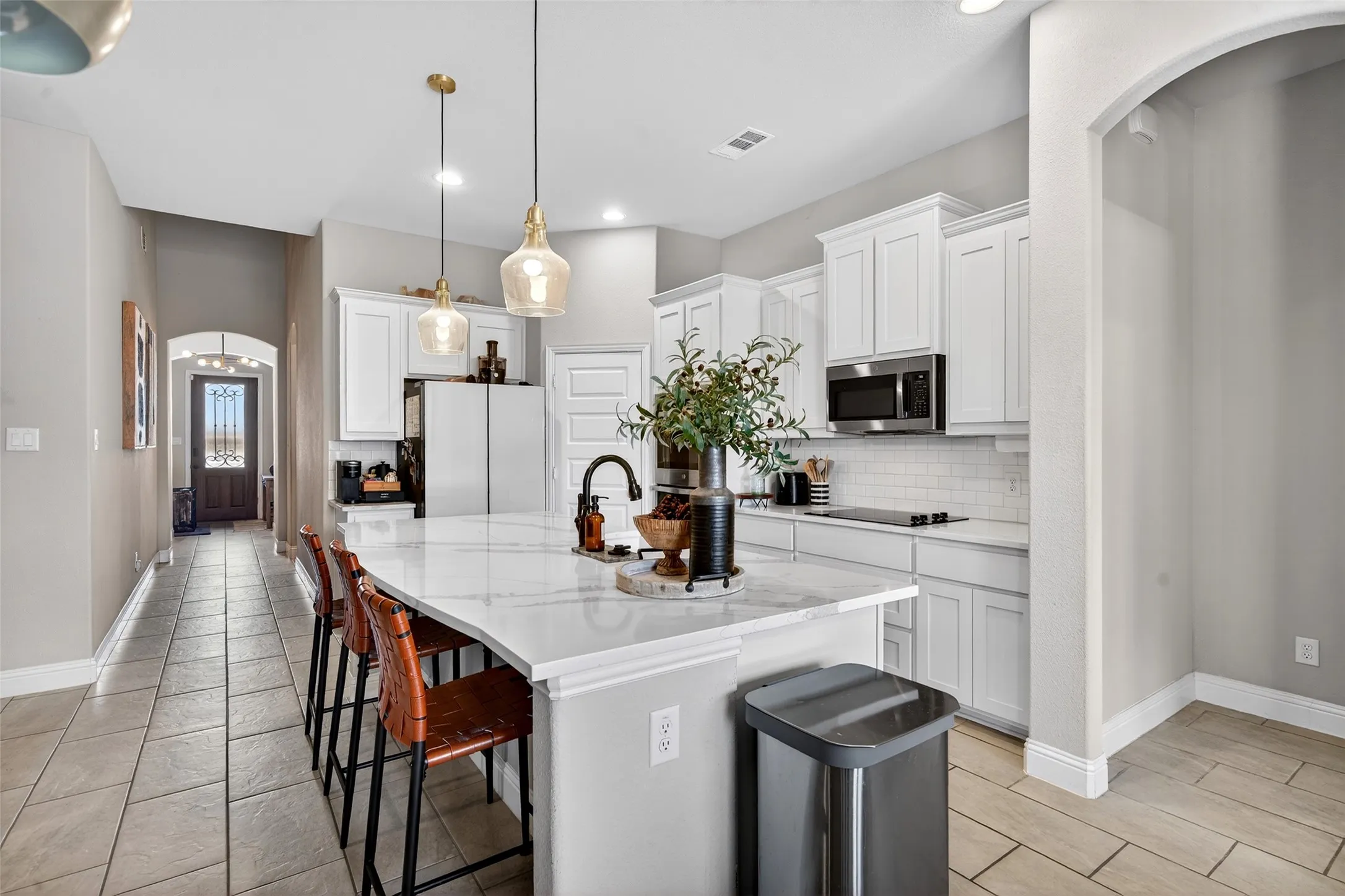 Kitchen featuring a large island with a light-toned countertop, white cabinetry, a built-in microwave, and a subway tile backsplash