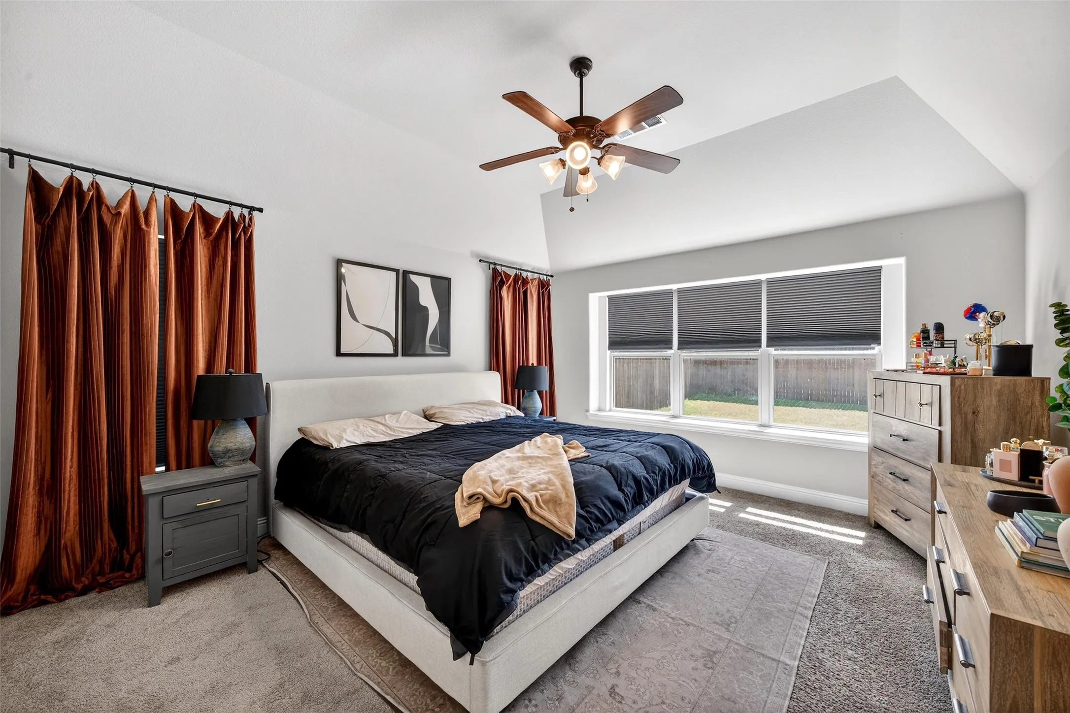 Vaulted ceiling with a ceiling fan, plush carpeting, triple windows with roller shades, and multiple windows with curtain rods