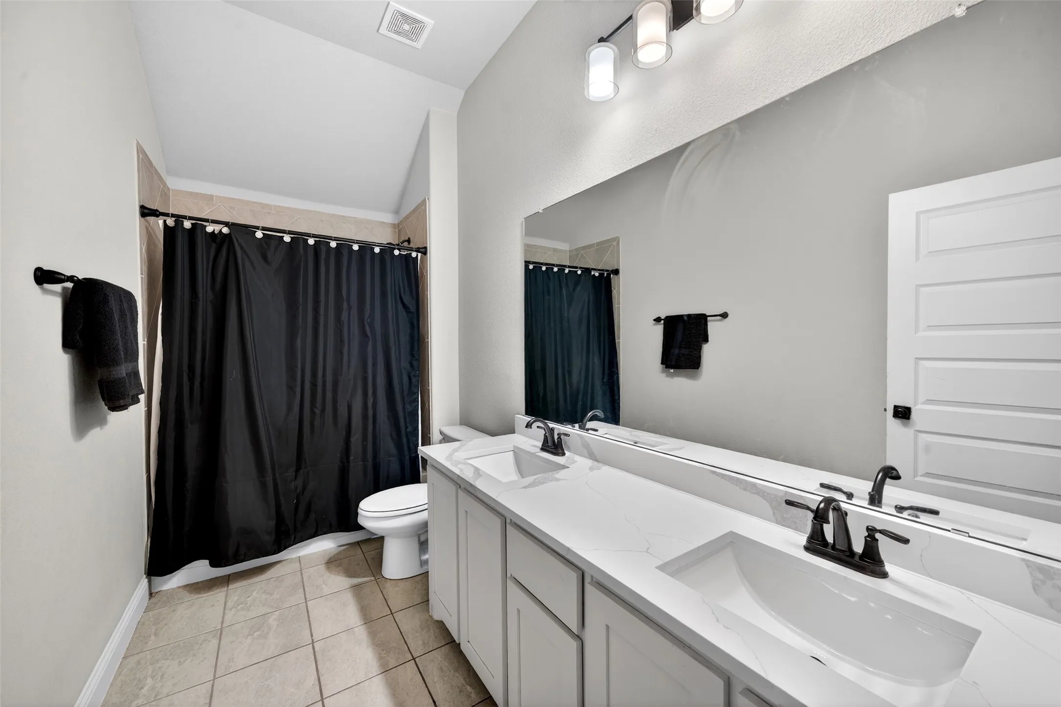 Double vanity with integrated sinks, expansive wall-mounted mirror, matte black fixtures, tile flooring, and a shower/tub combination