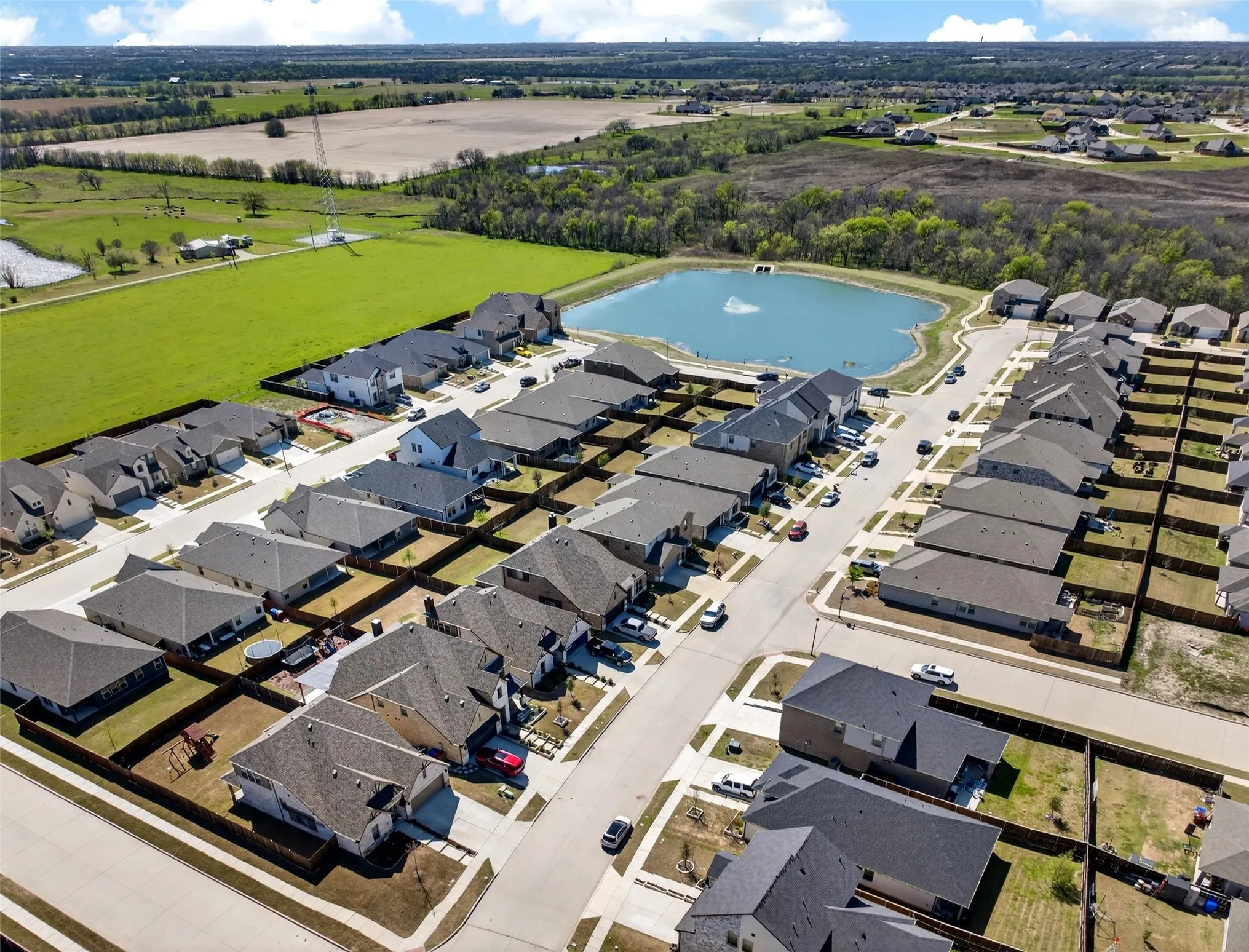 Community with a central pond feature, surrounded by residential properties, green spaces, and paved streets