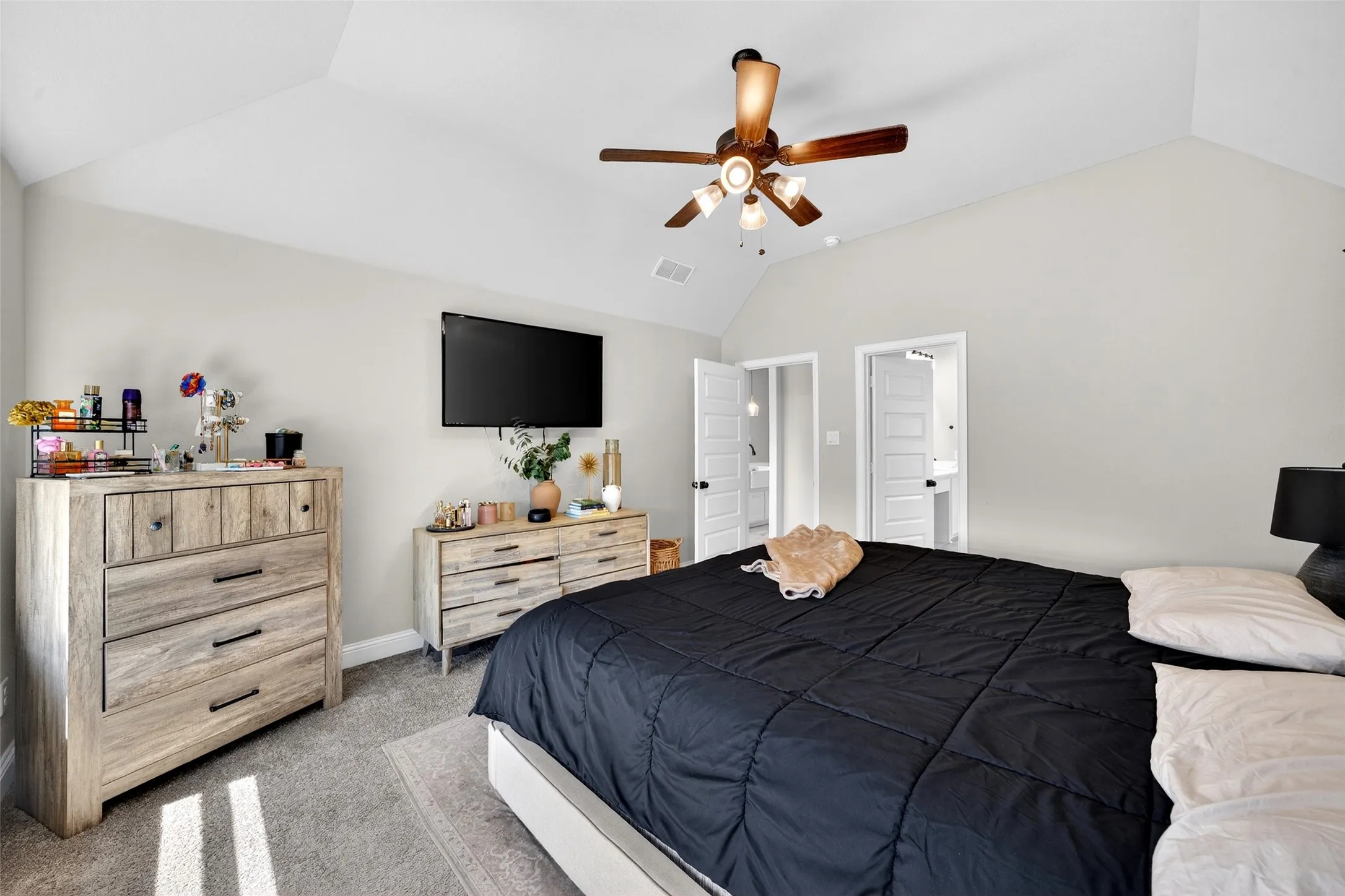 Vaulted ceiling, ceiling fan with light fixture, wall-mounted television, light gray wall paint, and gray carpet
