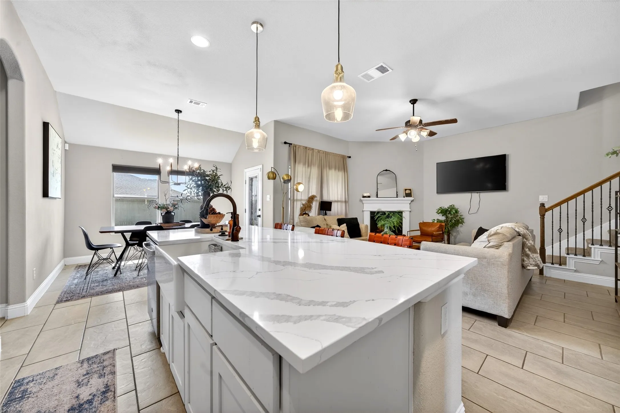Kitchen island with a white countertop and farmhouse sink, wood-finish flooring, staircase with wrought iron balusters, and a fireplace with a white mantel