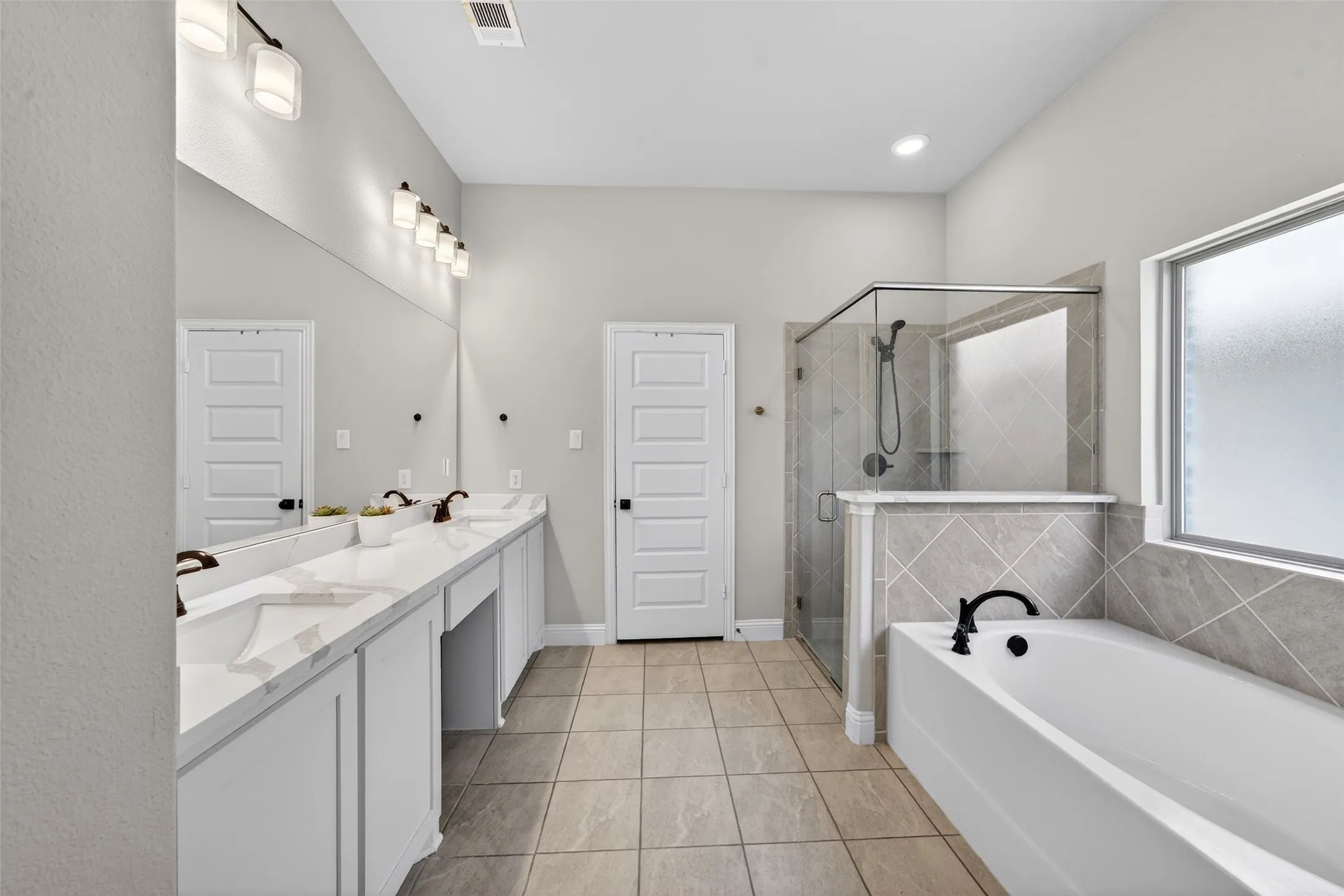Double vanity with undermount sinks, a built-in shower with glass enclosure, a separate soaking tub, and tiled flooring