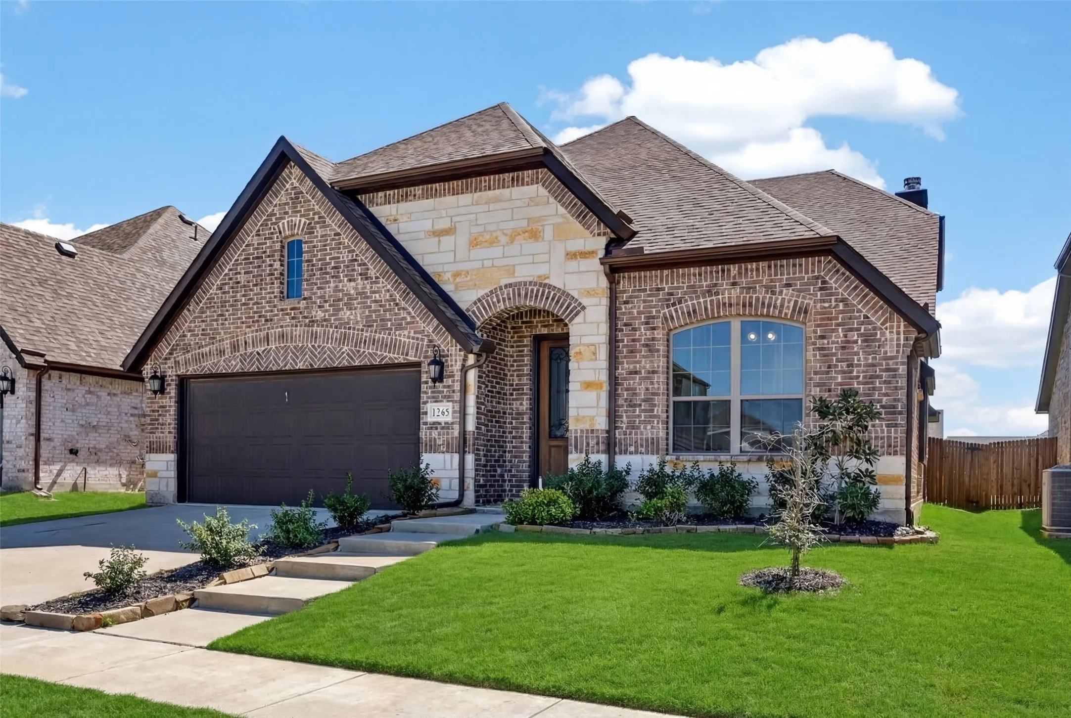 Brick and stone facade, arched entryway, multi-paned windows, attached two-car garage, and established landscaping