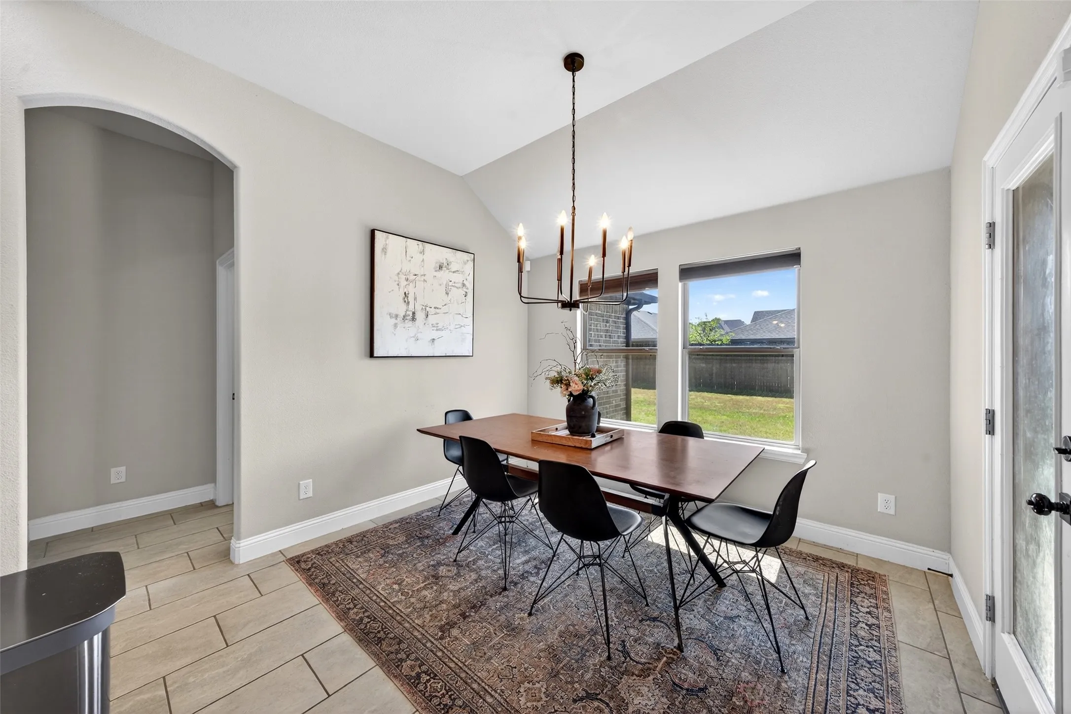 Vaulted ceiling with a chandelier, tile flooring, and an arched entryway