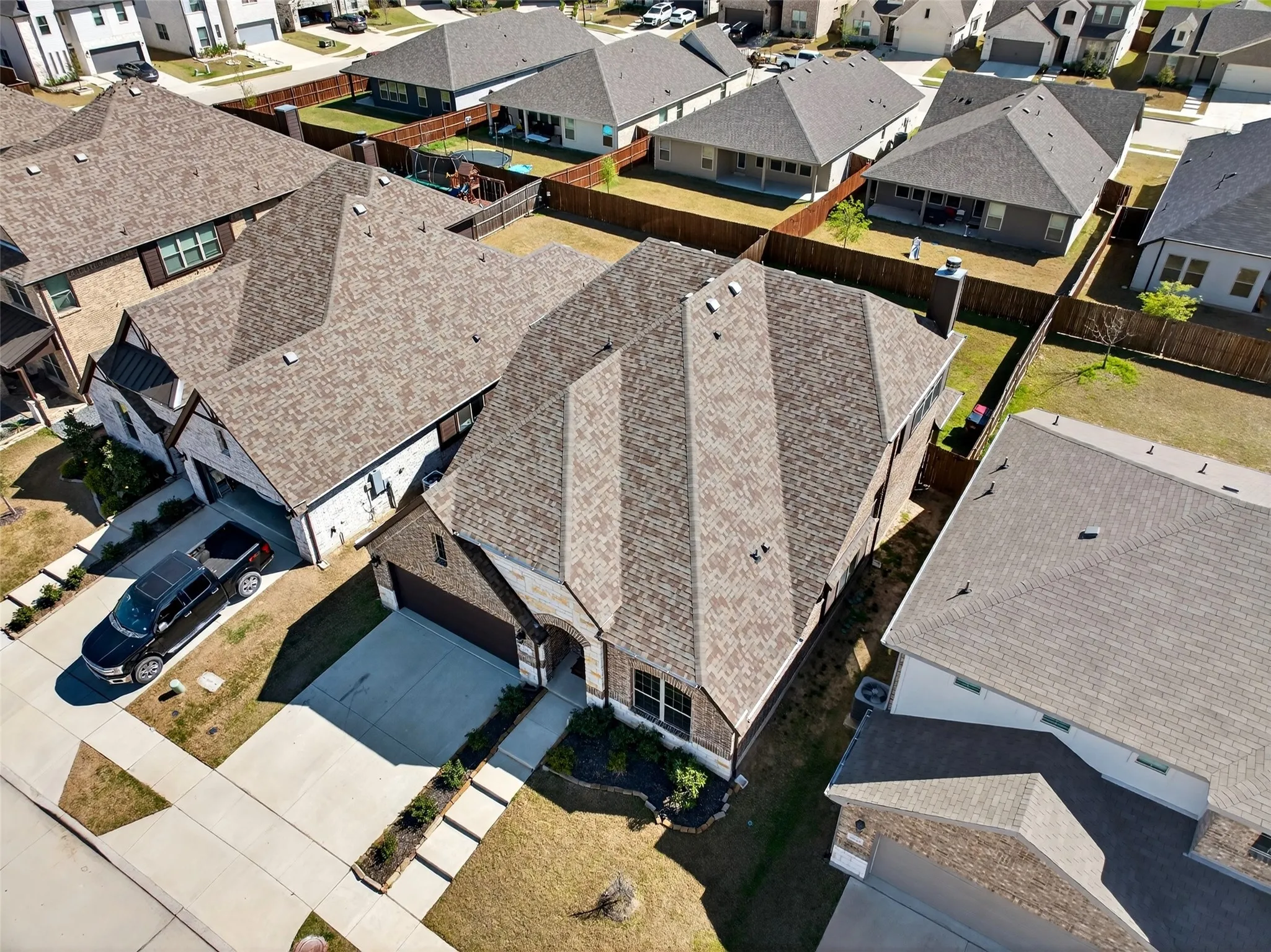 Aerial view highlighting the property's roofline, attached garage, concrete driveway, and front yard landscaping