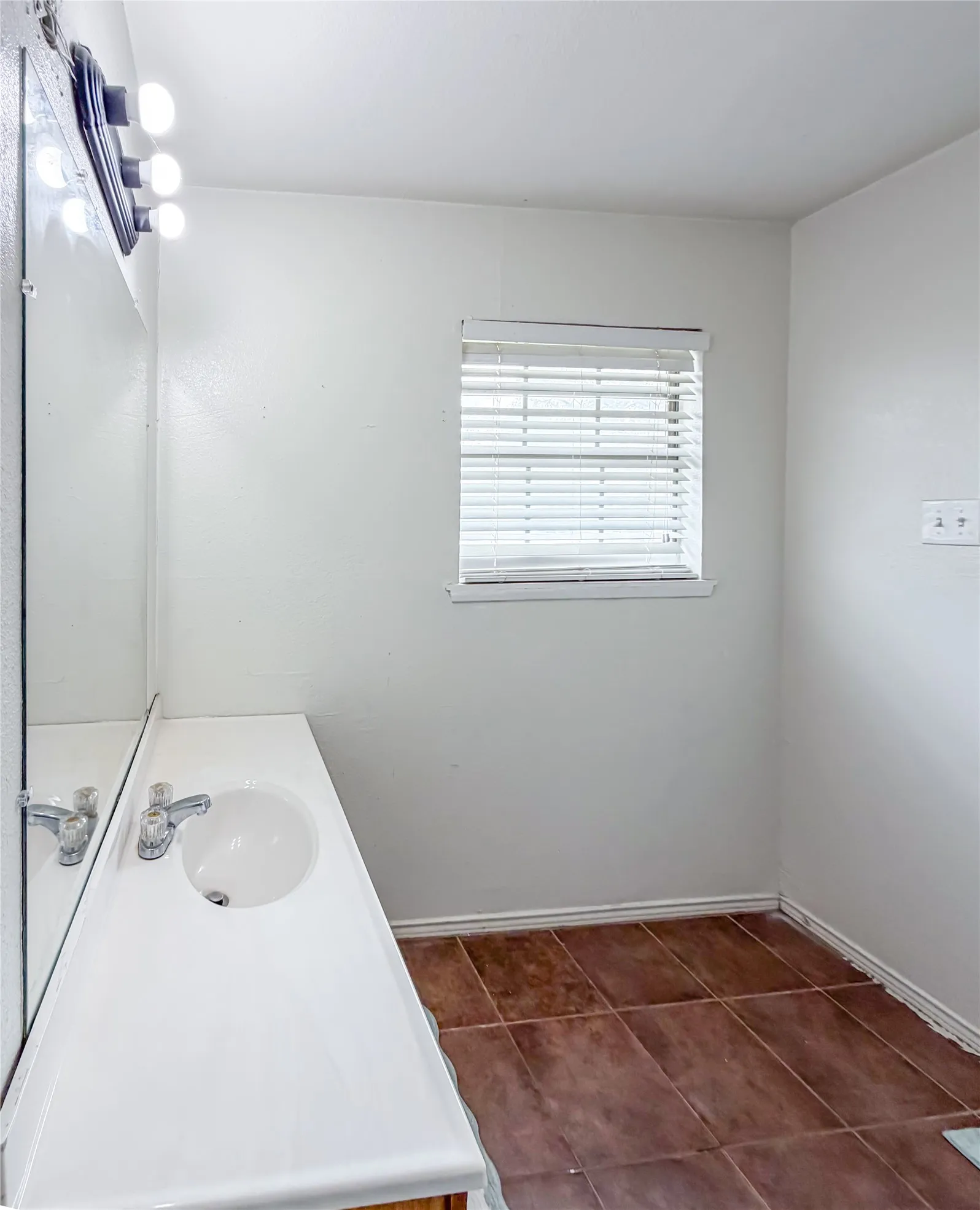 White vanity with integrated sink, chrome faucet, wall-mounted mirror, and overhead lighting