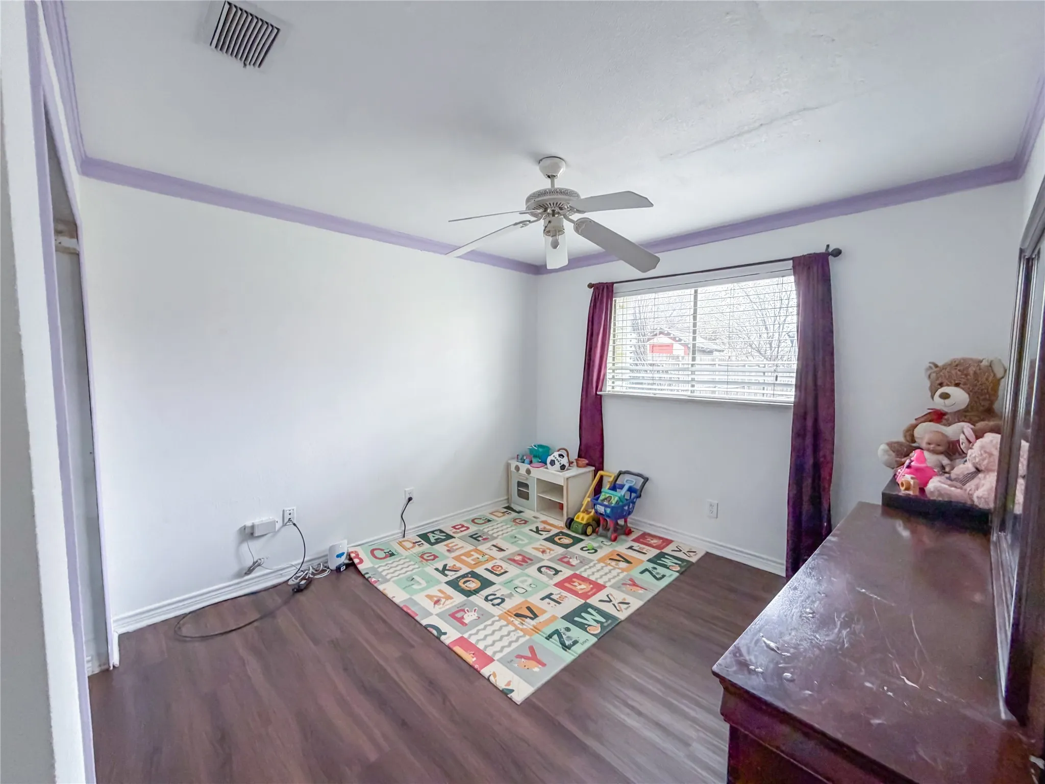 Wood-finish flooring, ceiling fan, window with blinds, and white walls with decorative trim