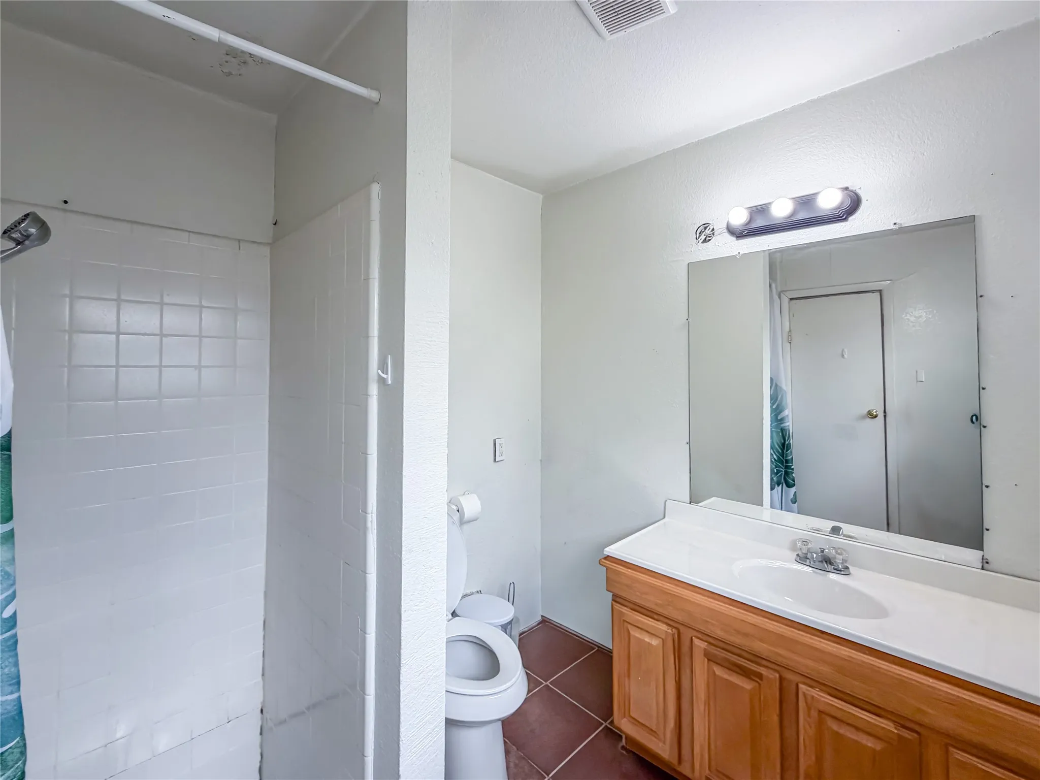 White tiled shower, wood-finish vanity with countertop, integrated sink, and large wall-mounted mirror