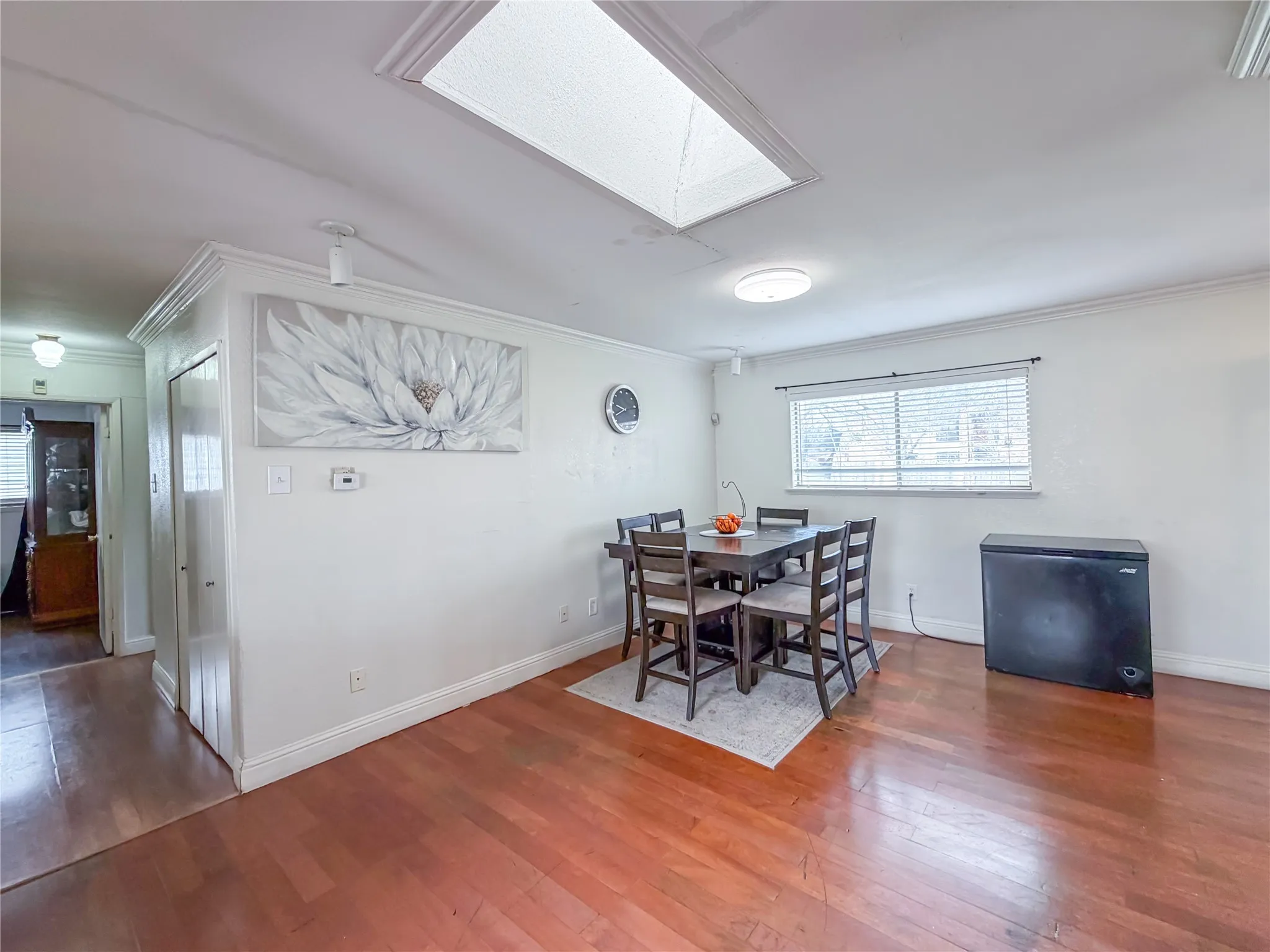 Wood-finish flooring, overhead skylight, recessed lighting, crown molding, and window with blinds