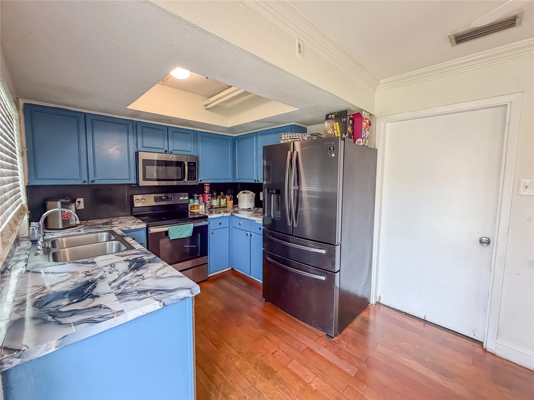 Kitchen featuring blue cabinetry, stainless steel appliances, a double basin sink, marble-patterned countertops, and wood-finish flooring