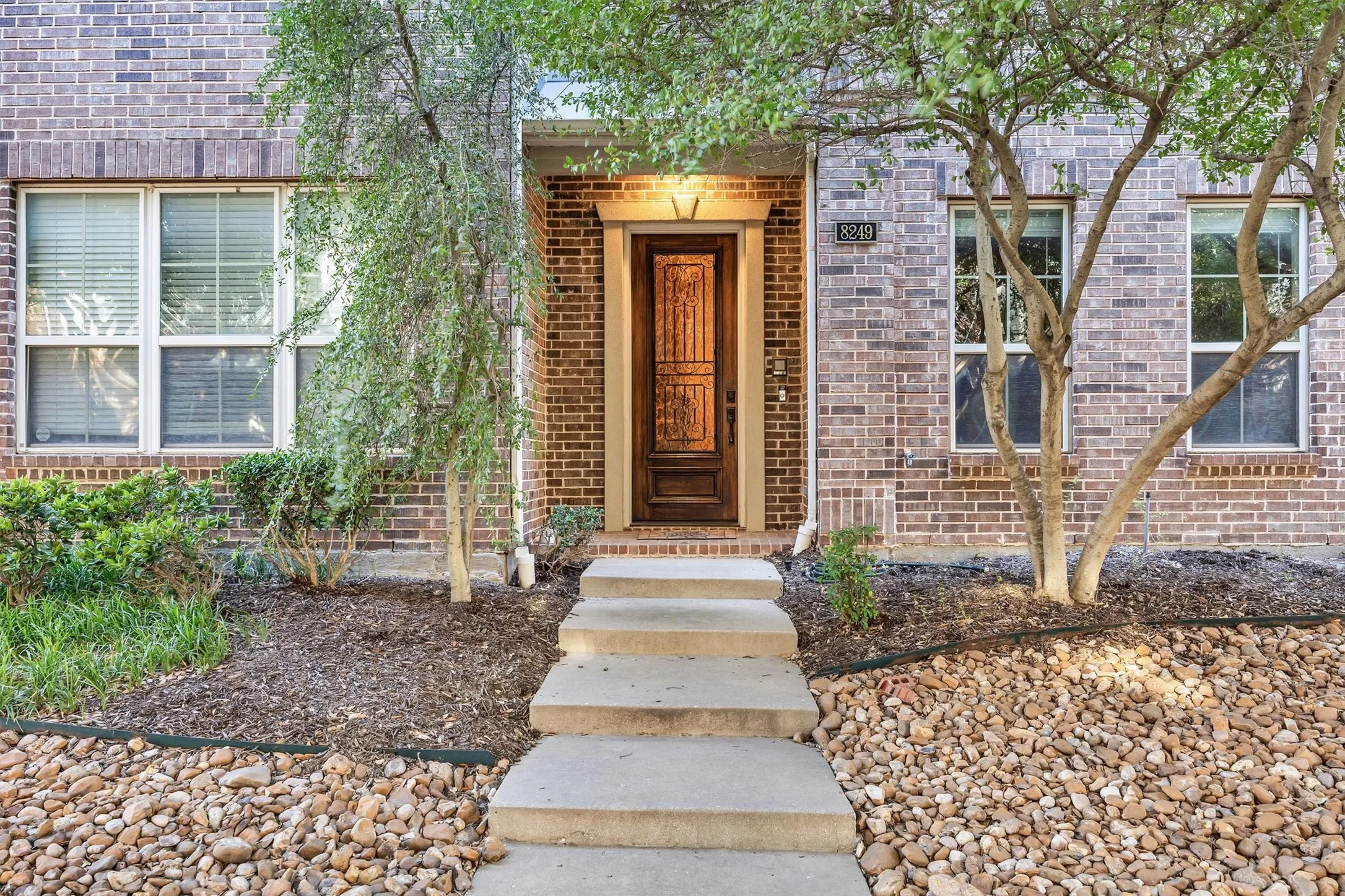 Brick exterior with multiple windows, a wood-paneled front door, and a concrete pathway leading to the entrance