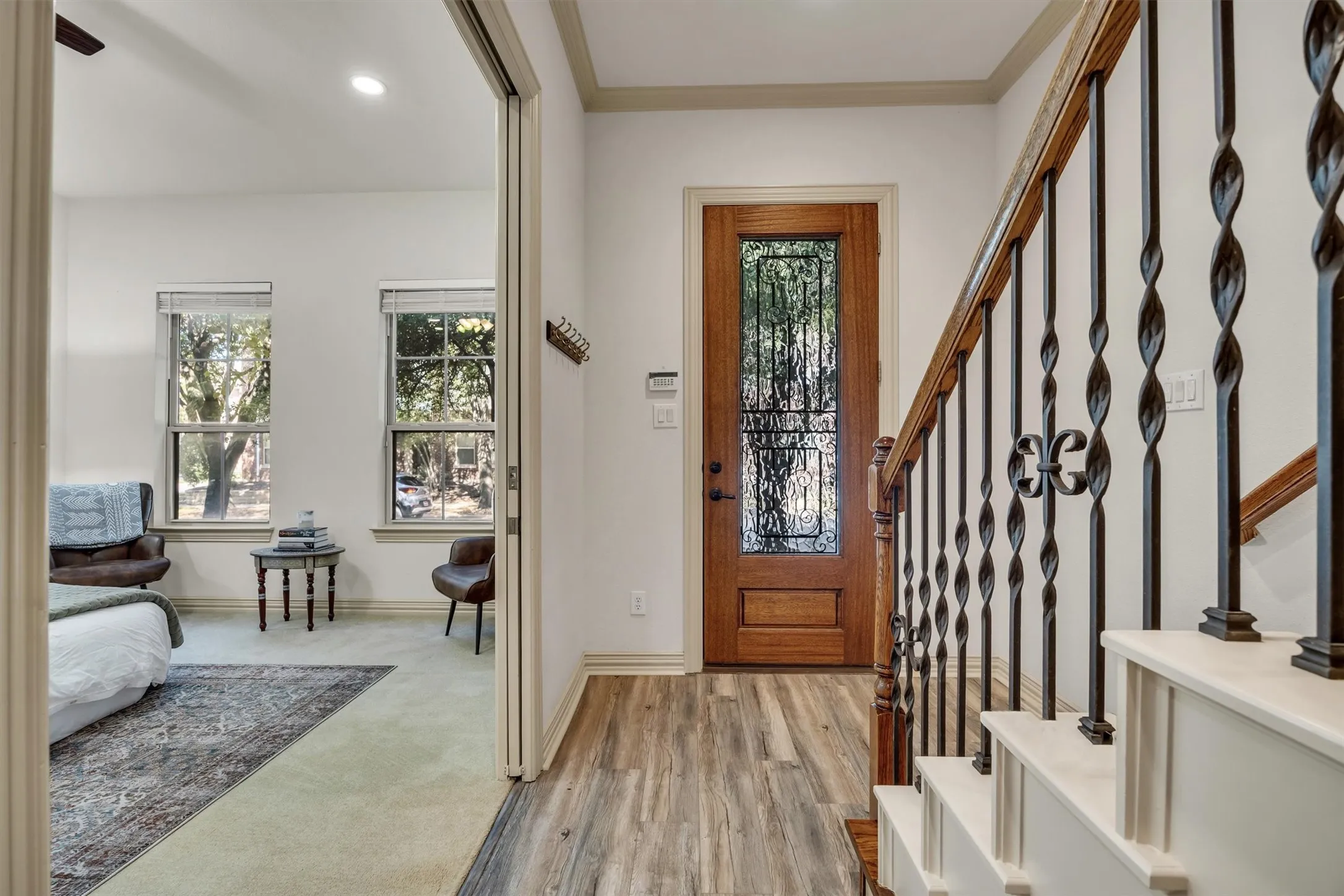 Wood-finish flooring, staircase with wrought iron balusters and wood handrail, solid wood entry door with decorative glass, and recessed lighting