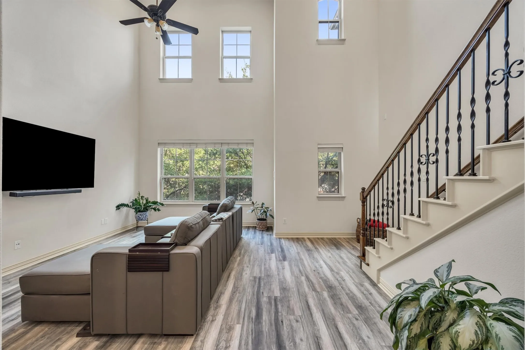 High ceilings, wood-finish flooring, staircase with wrought iron balusters, multiple windows, and a ceiling fan