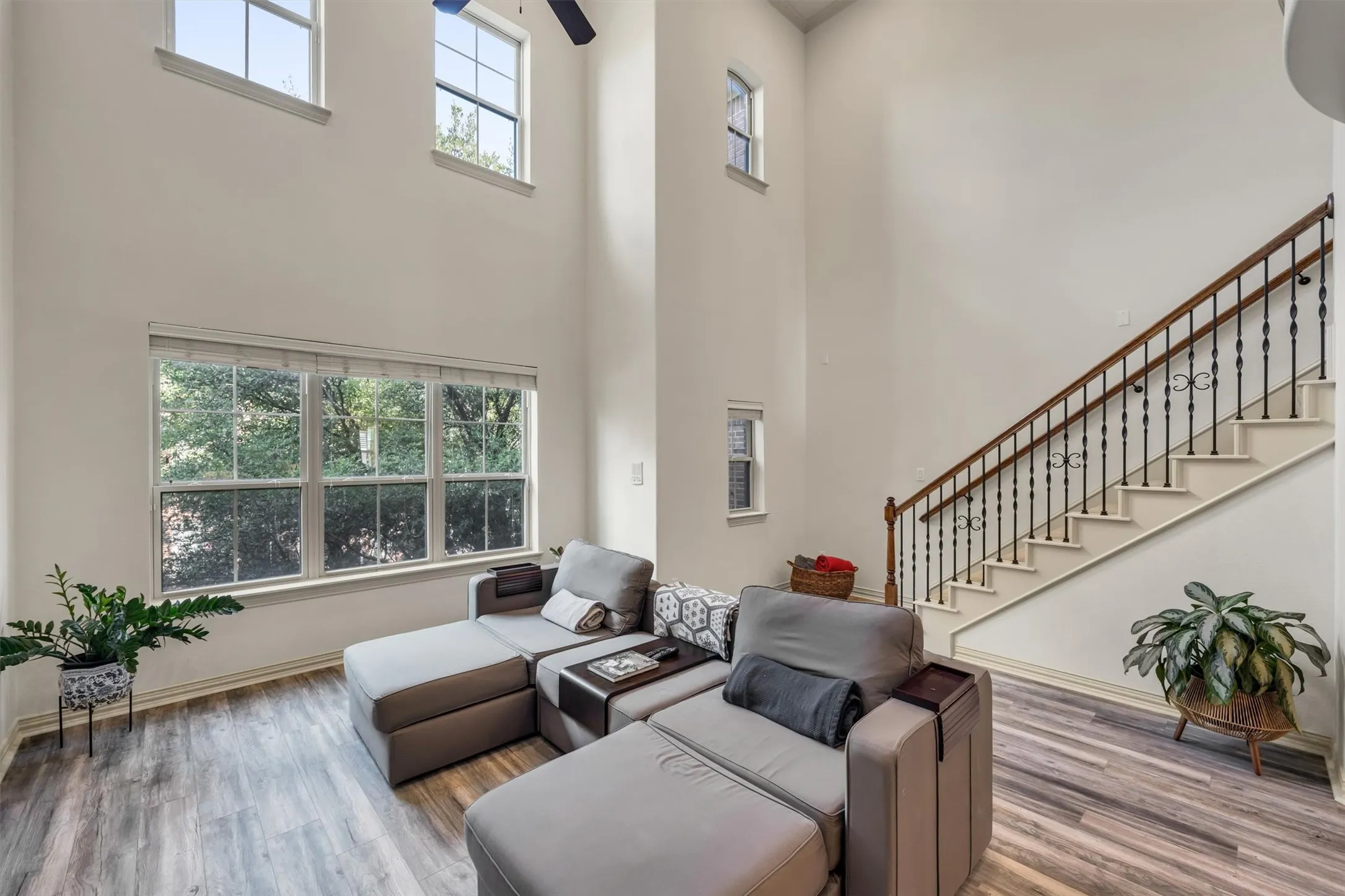 High ceilings with upper windows, large picture windows, wood-finish flooring, staircase with wrought iron balusters and wood handrail, ceiling fan