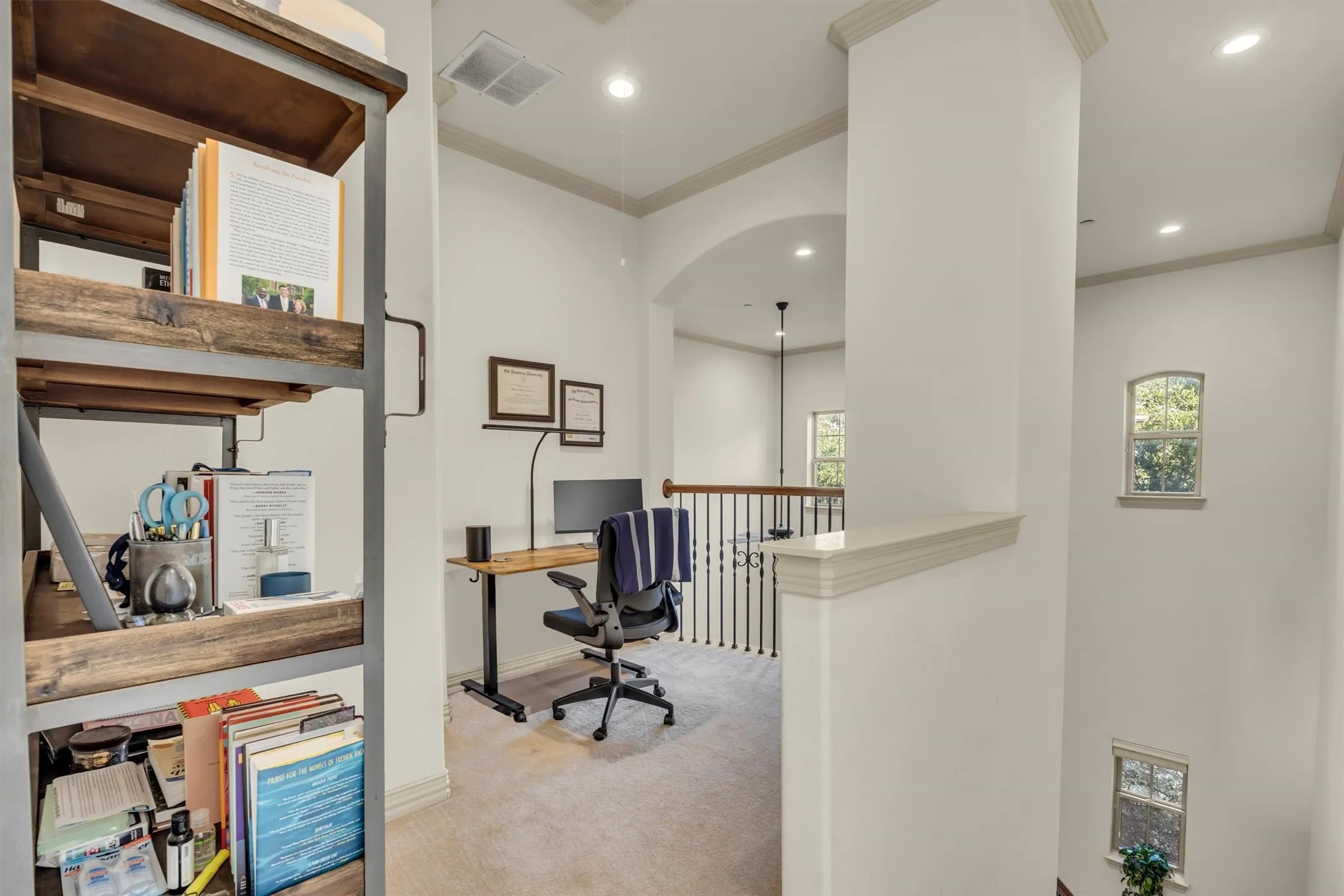 Carpeted loft area featuring a dark wood-finish desk, recessed lighting, arched doorway, and white painted balusters