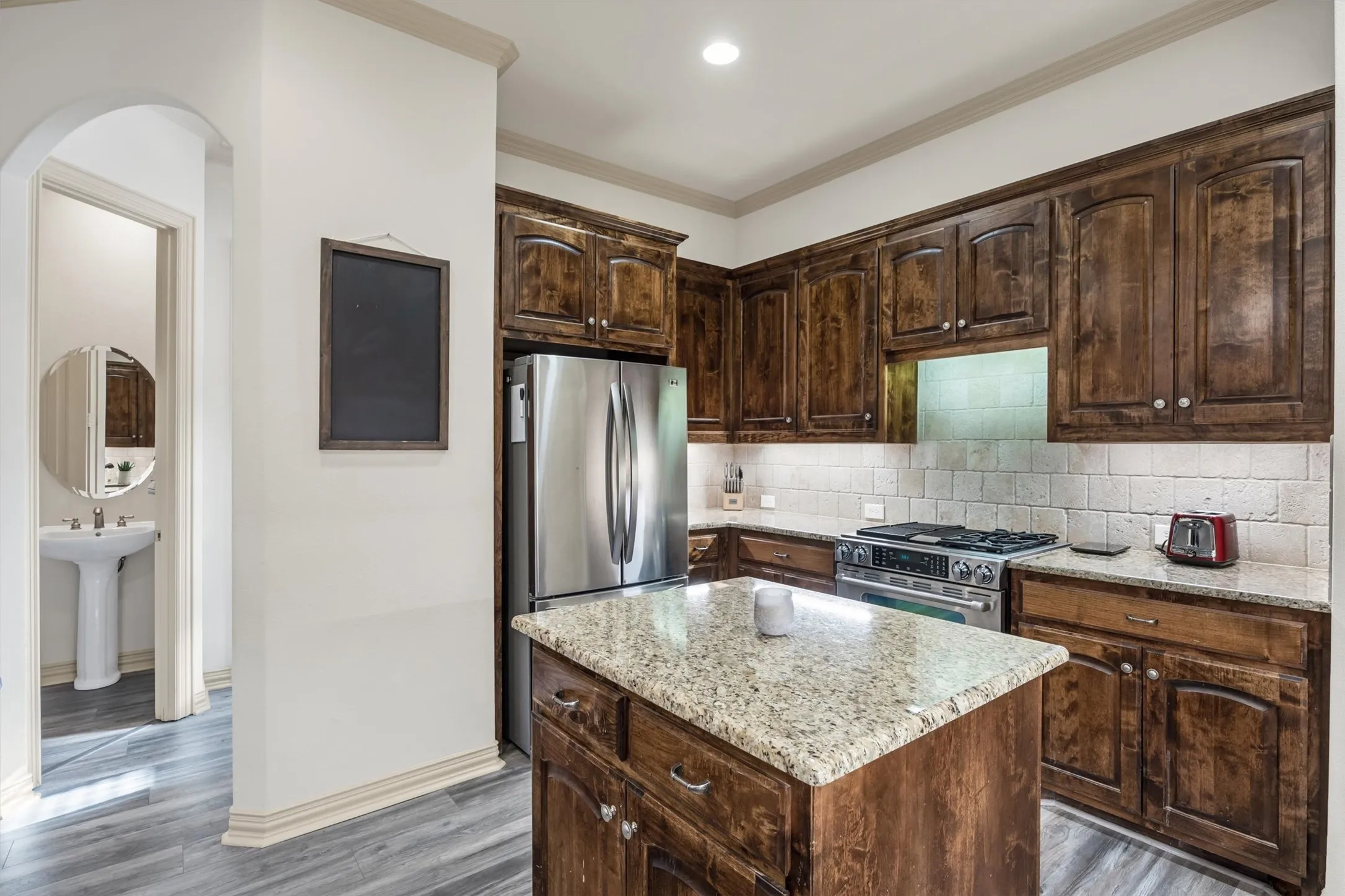 Kitchen featuring wood-finish cabinetry, stainless steel appliances, a stone countertop island, stone countertops, and a subway tile backsplash