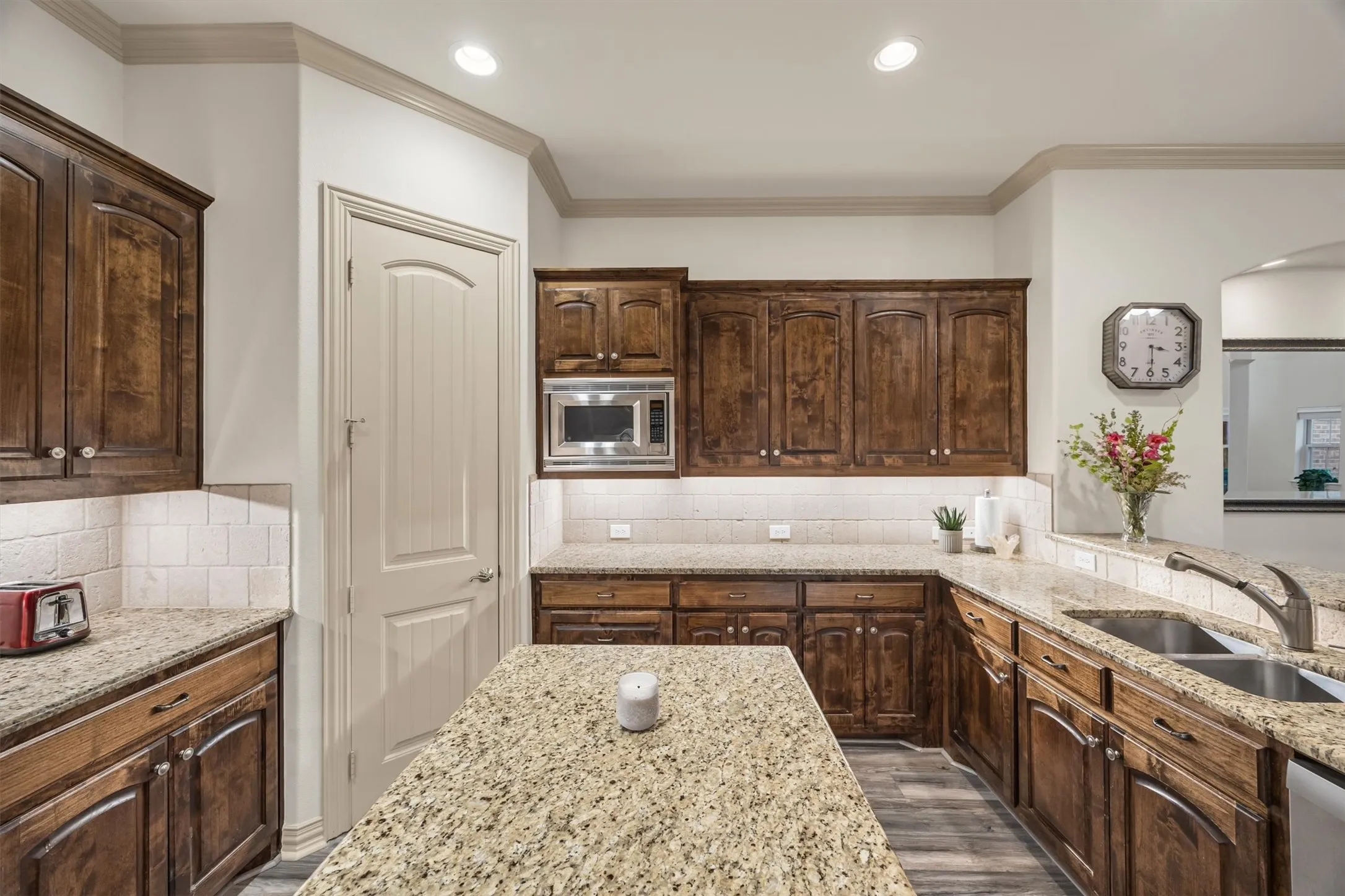 Kitchen featuring wood-finish cabinetry, light speckled countertops, a double basin stainless steel sink, and a tiled backsplash