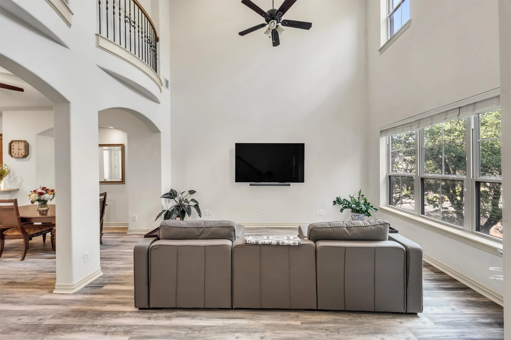Two-story living area featuring a ceiling fan, wood-finish flooring, and a bank of large windows with blinds