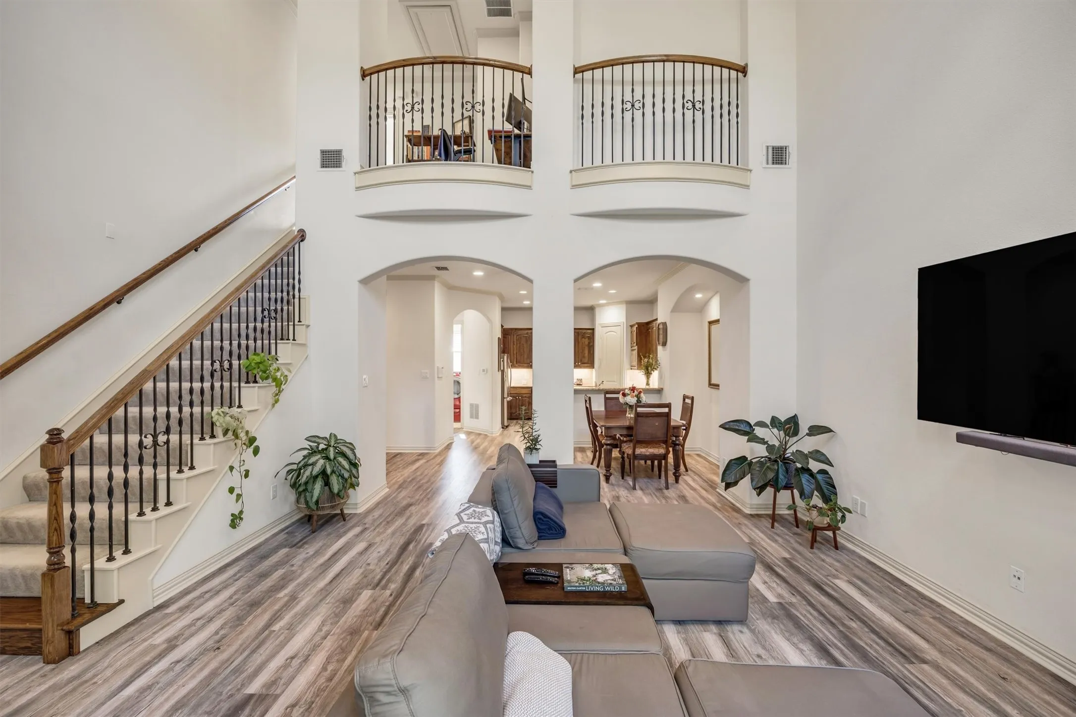 Two-story living area featuring wood-finish flooring, a carpeted staircase with wood and iron banisters, and arched doorways