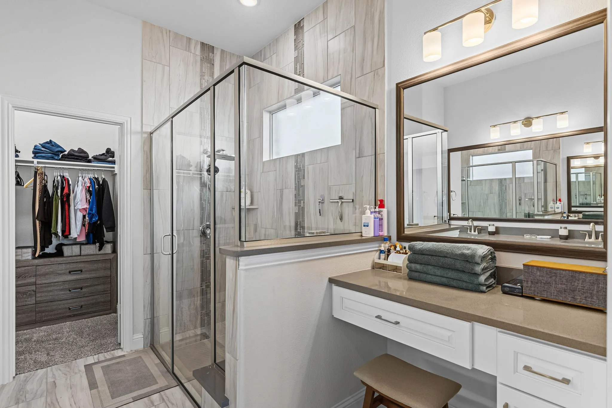 Walk-in closet with built-in storage, glass-enclosed shower with tile surround, dual vanity with undermount sinks, and a dedicated vanity counter with storage
