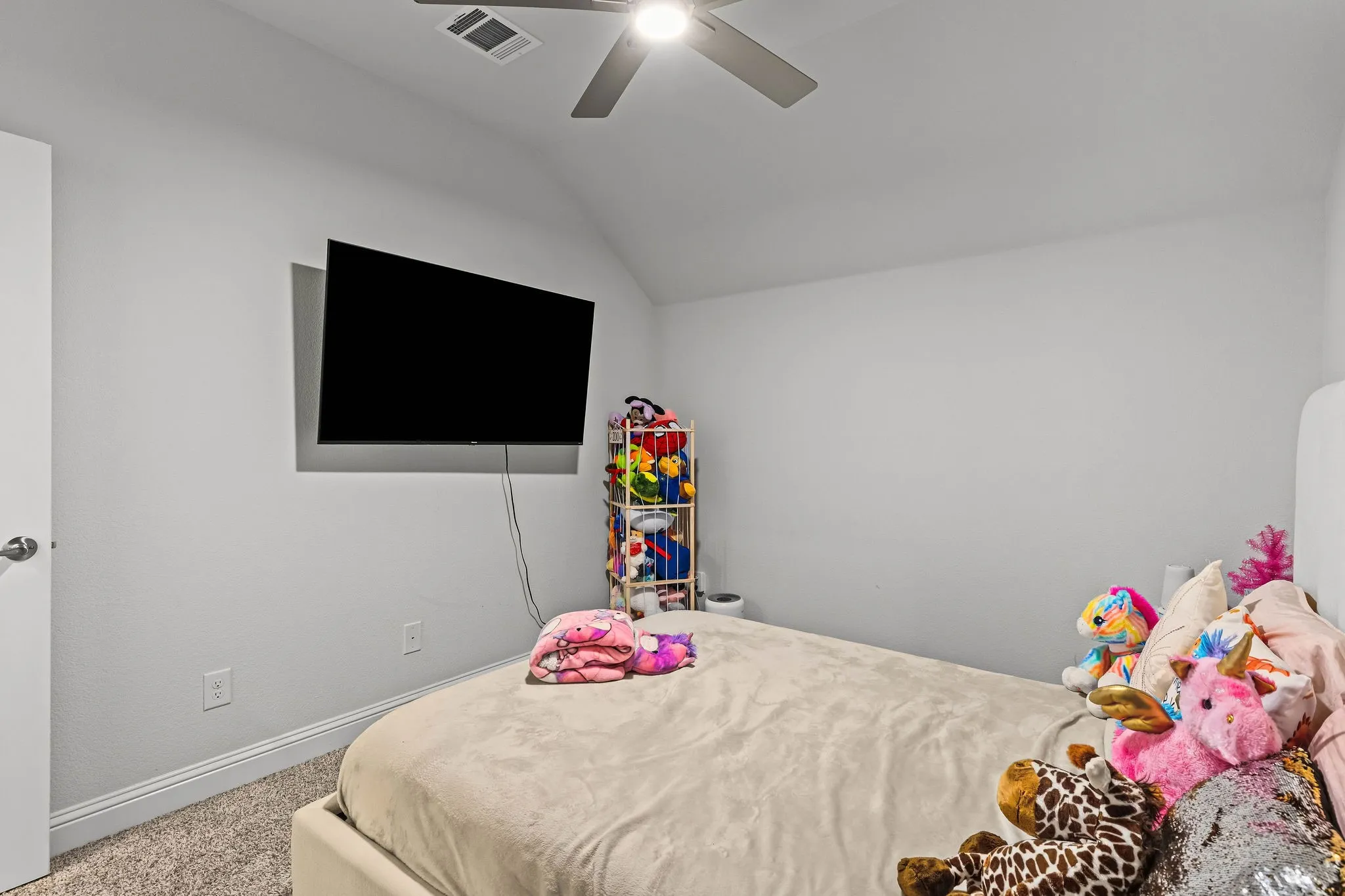 Sloped ceiling featuring a ceiling fan with integrated lighting, wall-mounted display, and carpeted flooring