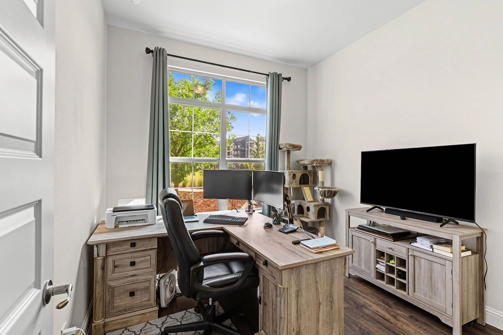 Hardwood-style flooring, white paneled door, large window with ample natural light, neutral wall paint, and crown molding