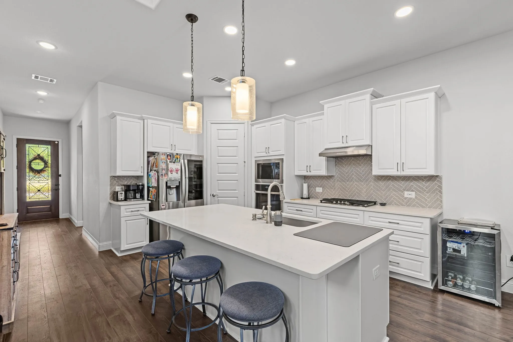White shaker cabinetry, wood-finish flooring, quartz countertops, herringbone tile backsplash, and stainless steel appliances