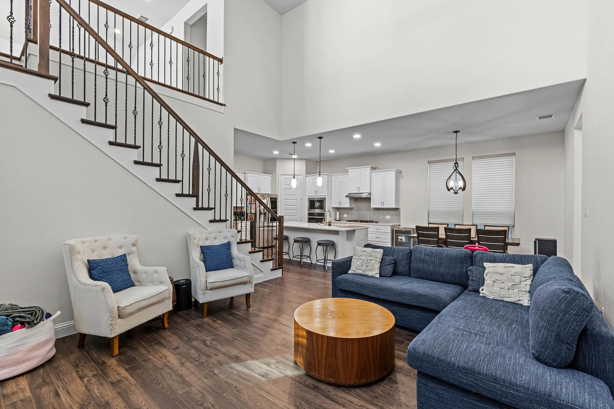 Wood-finish flooring, staircase with decorative wrought iron spindles, high ceilings, recessed lighting, and an open-concept kitchen with white cabinetry
