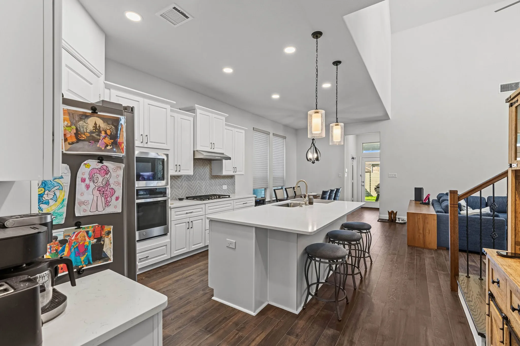 White shaker-style cabinetry, a kitchen island with seating, a chevron-patterned backsplash, stainless steel appliances, and dark wood-finish flooring