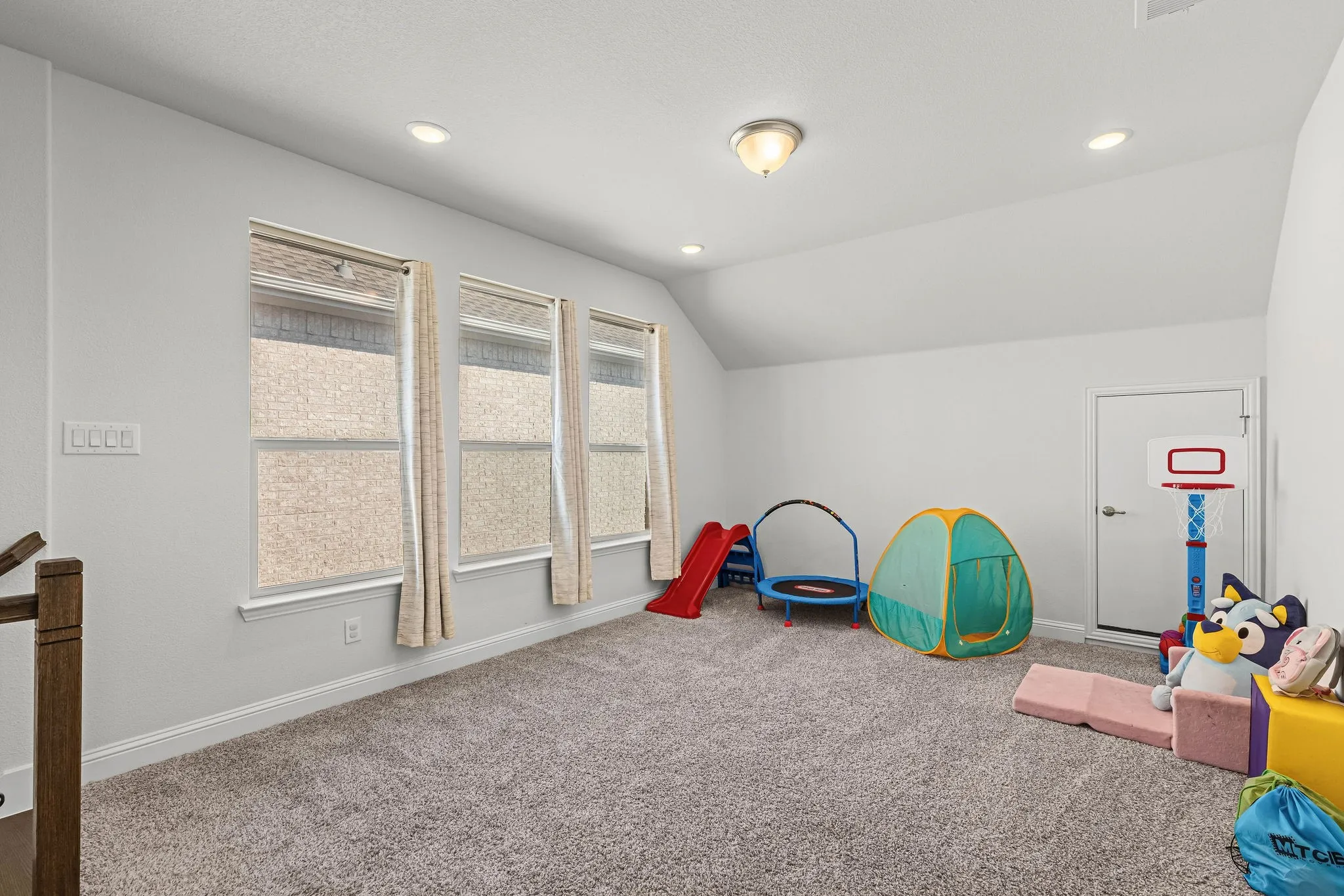 Carpeted room featuring three windows with blinds, recessed lighting, and a sloped ceiling