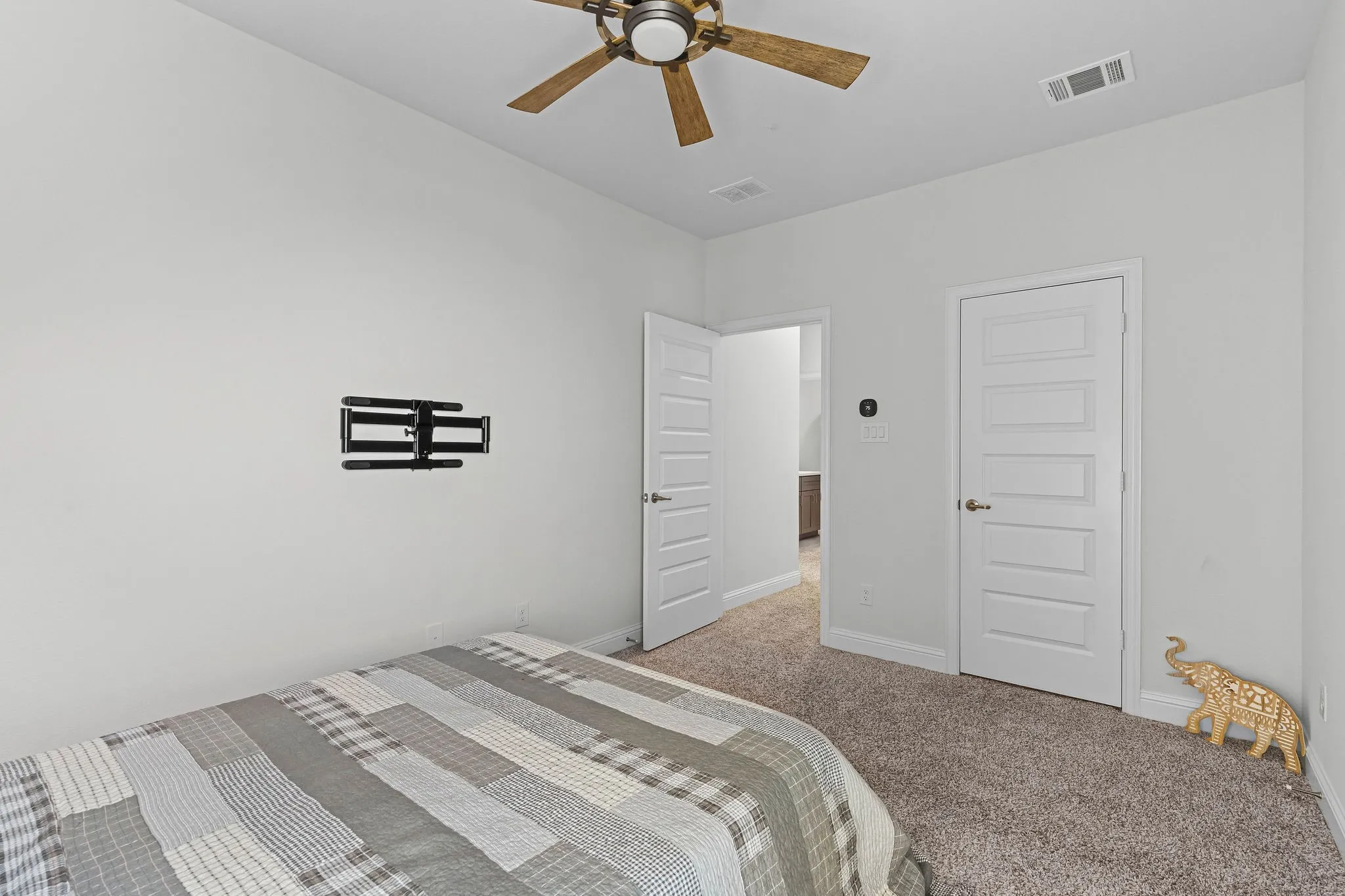 Carpeted flooring, white paneled doors, ceiling fan with wood-finish blades, and a mounted television bracket
