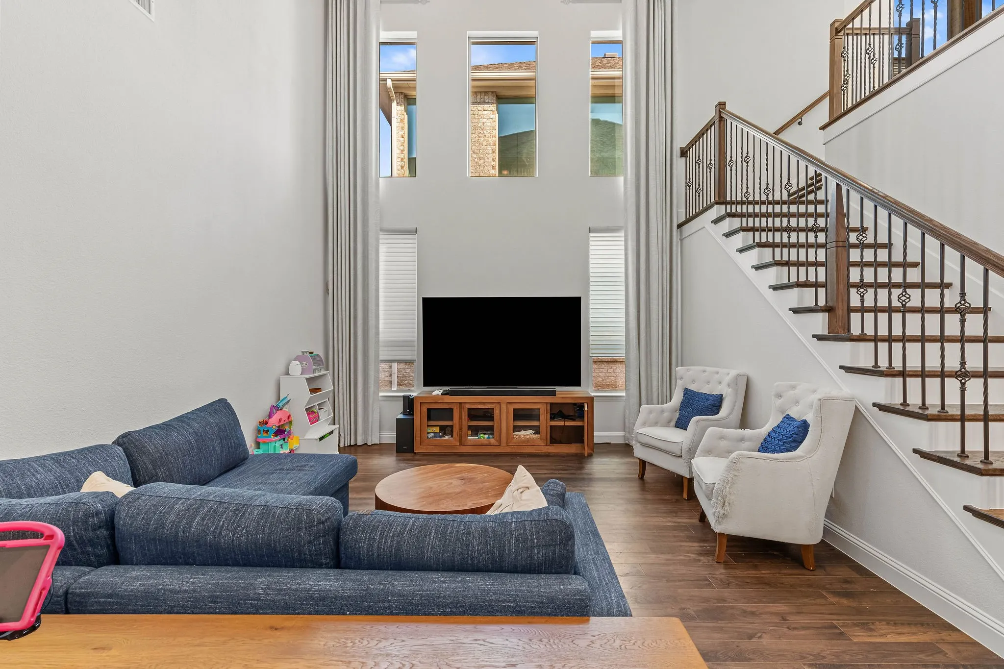 Two-story ceiling, wood-finish flooring, multiple upper-level windows, custom curtain panels, and a wood and wrought iron staircase