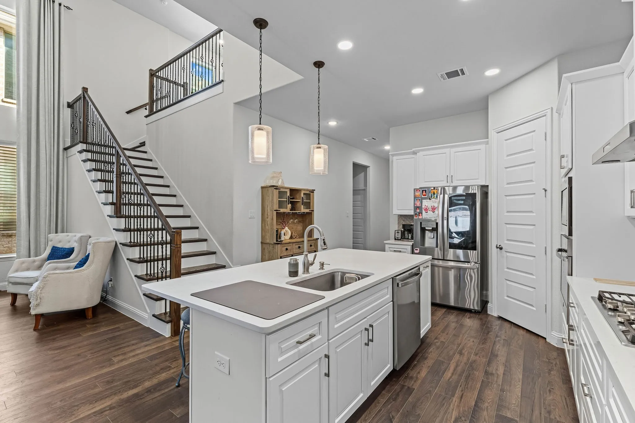 Kitchen featuring a large central island with an undermount sink, white cabinetry with silver hardware, stainless steel appliances, and wood-finish flooring