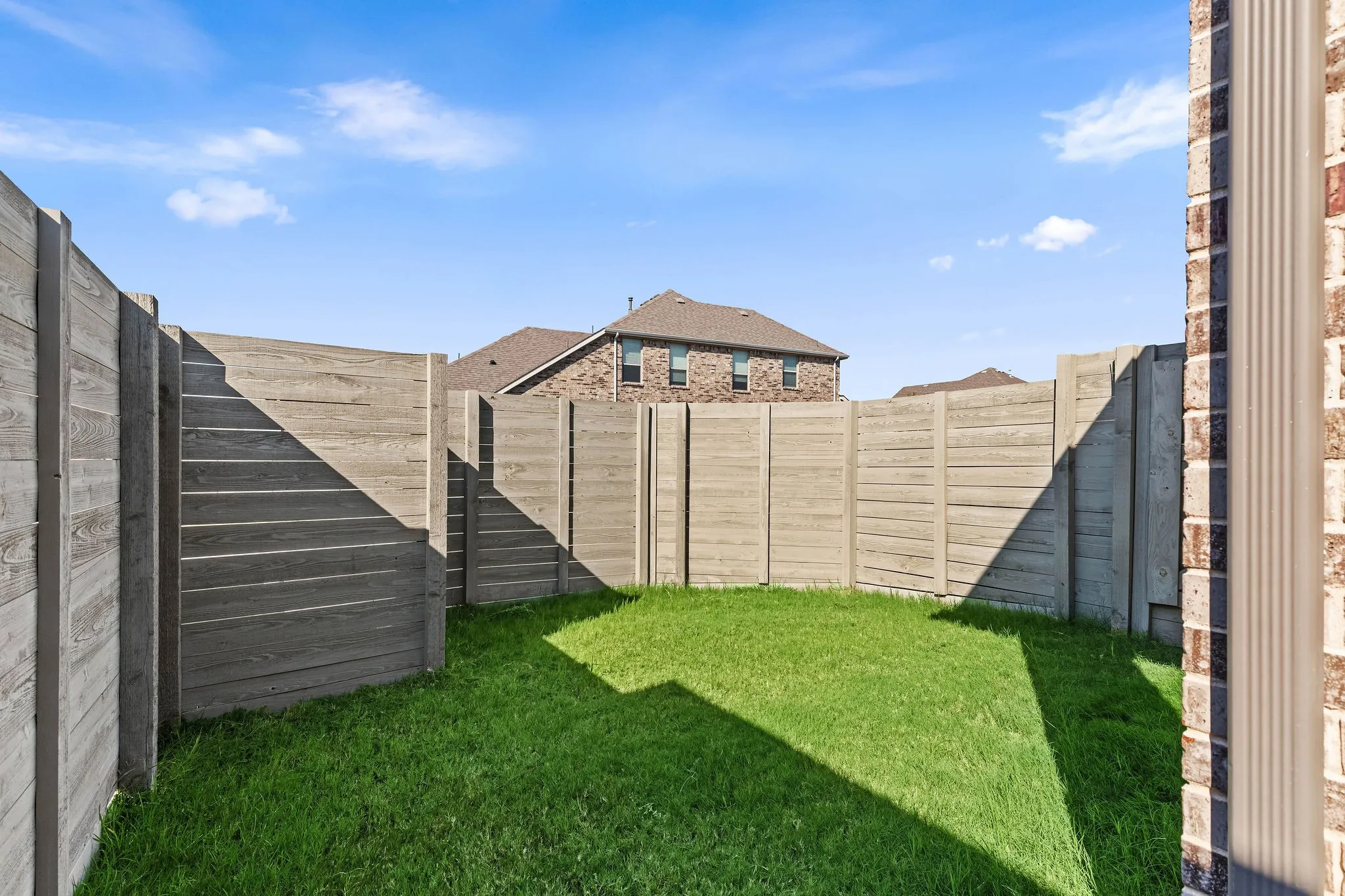 Enclosed backyard featuring a manicured lawn, concrete fencing, and a brick exterior wall with a rain gutter