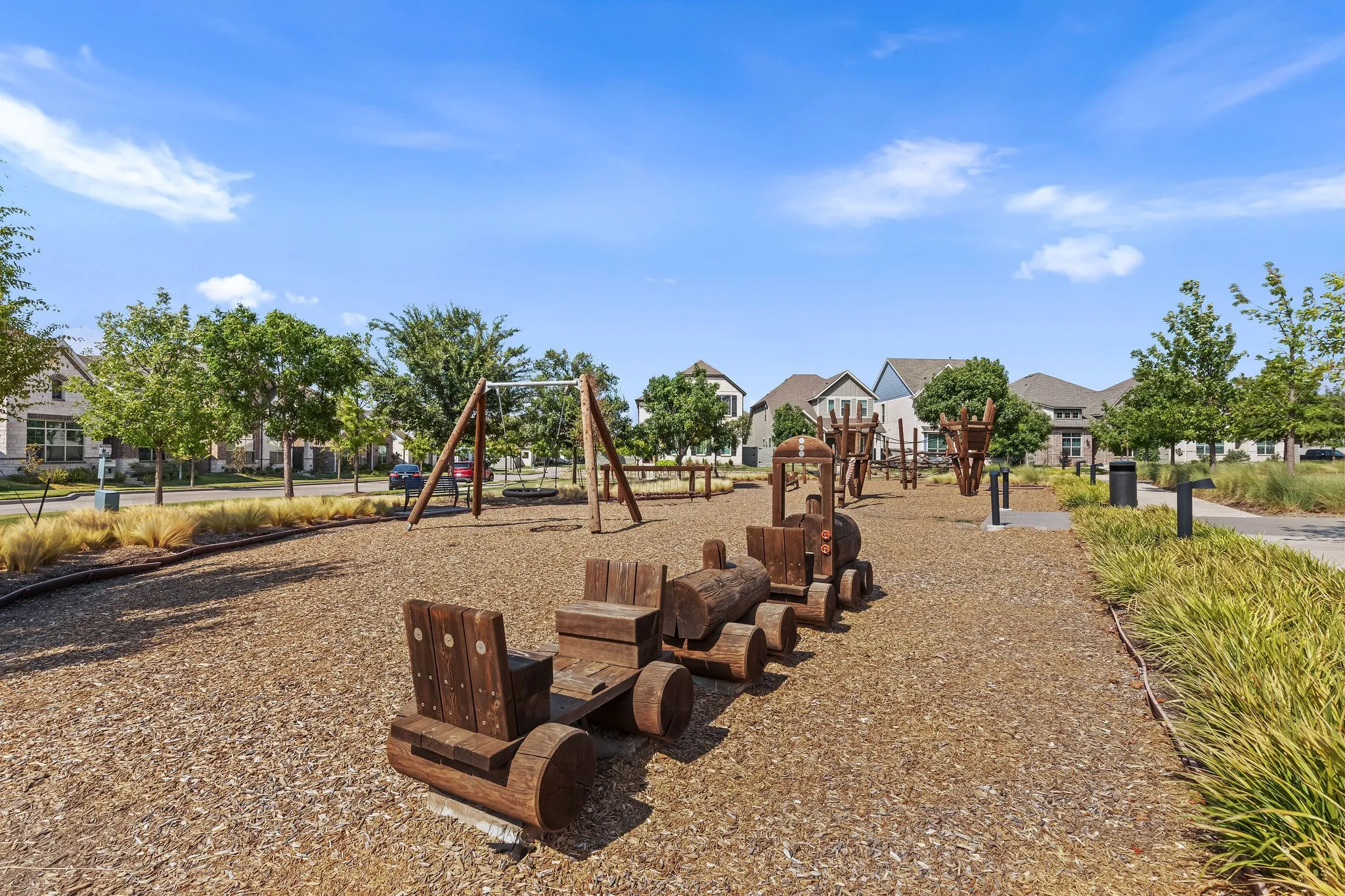 Community play area featuring a wooden train structure, swing set, and natural ground cover