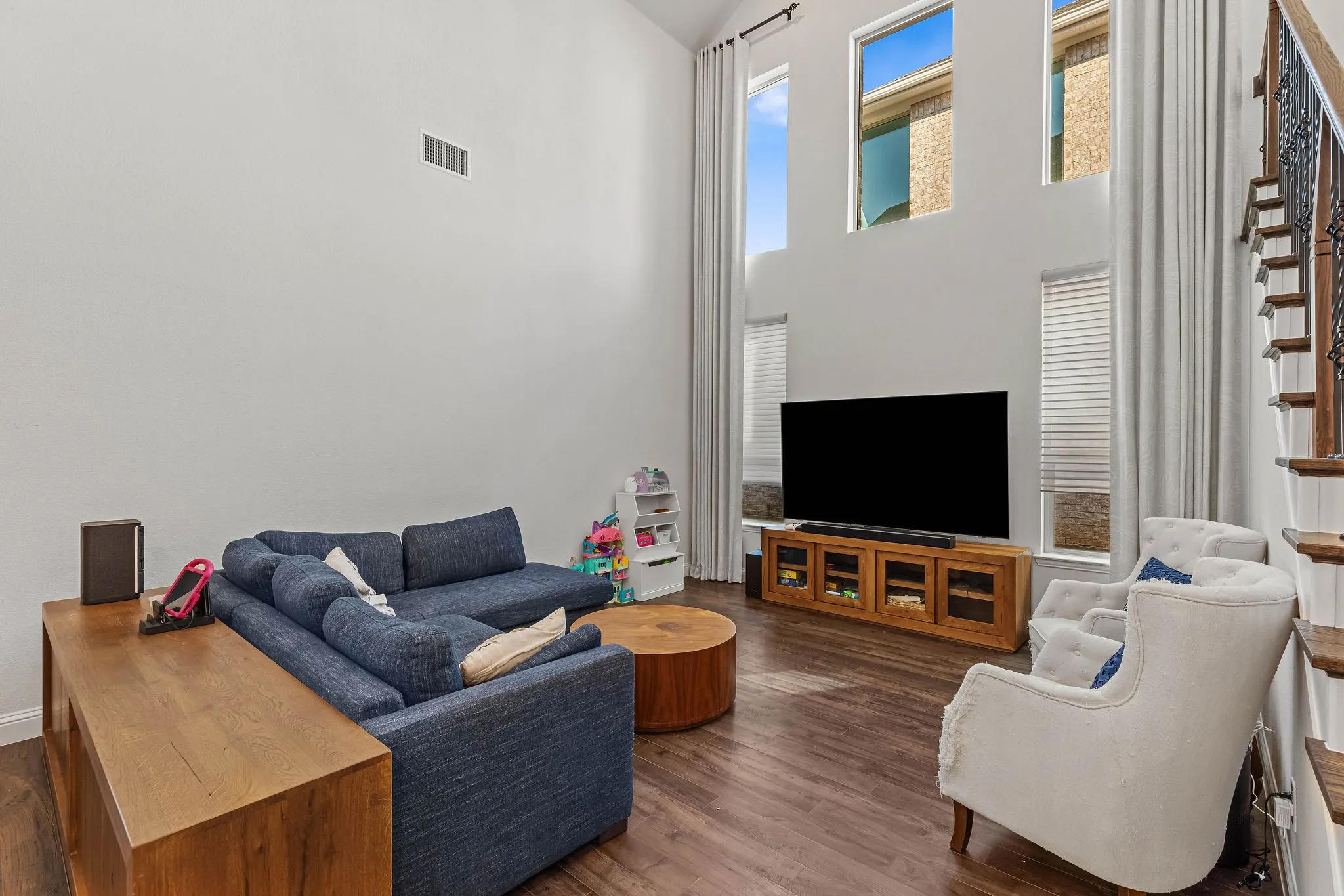 Two-story living area with high ceilings, multiple windows, wood-finish flooring, and a built-in media console