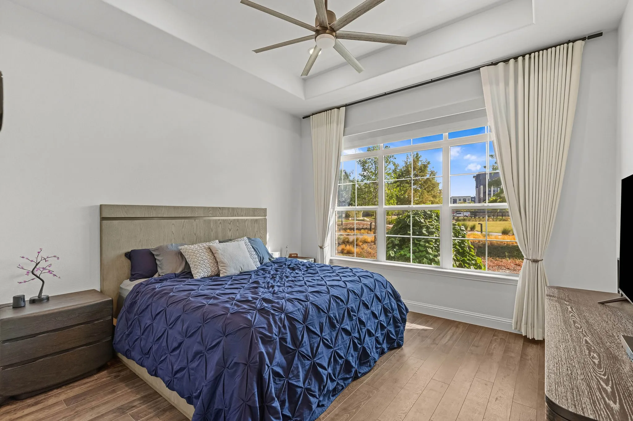 Tray ceiling with a ceiling fan, large multi-pane window, wood-finish flooring, and light-colored walls