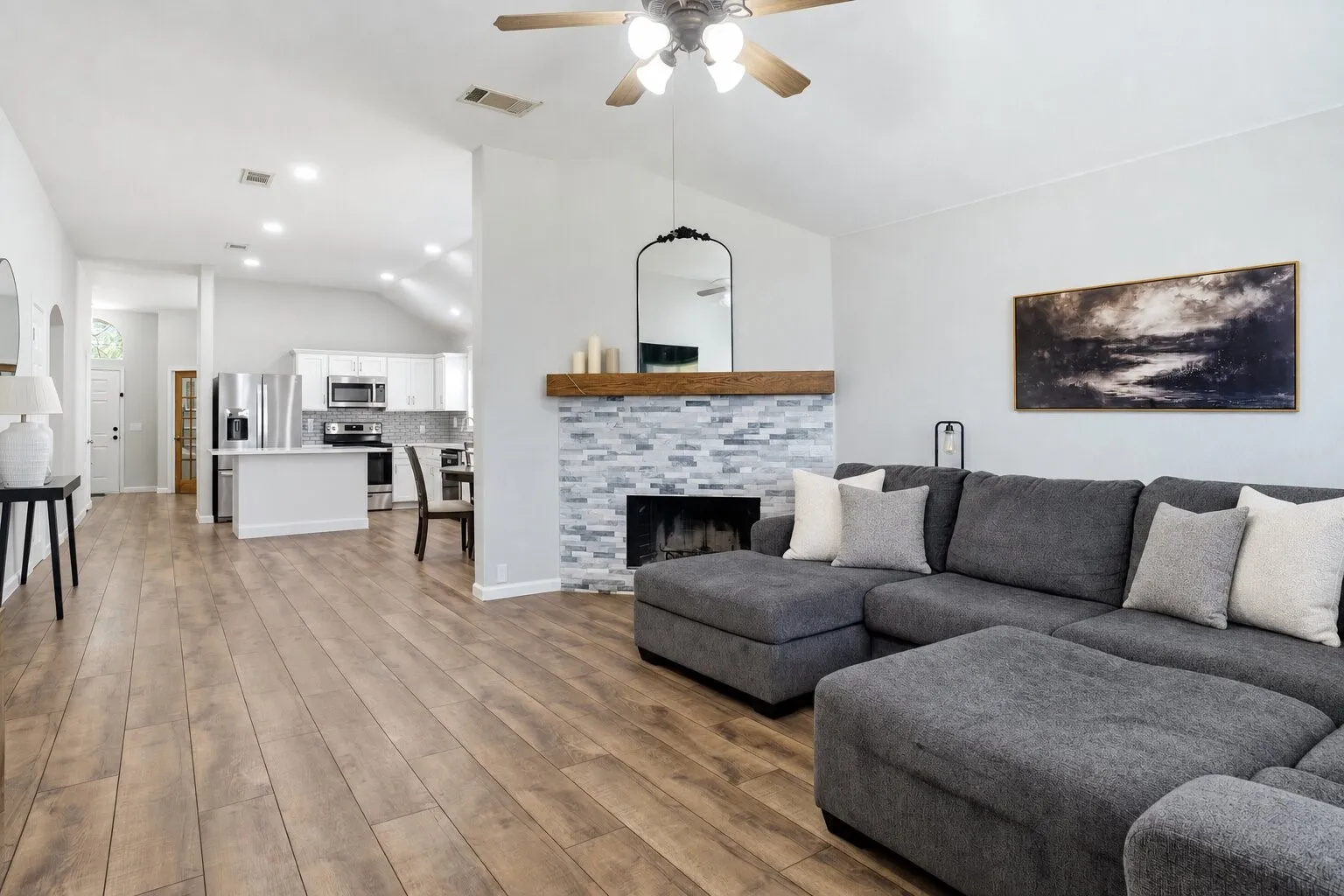 Open-concept living area featuring a vaulted ceiling, floor-to-ceiling stone fireplace, and seamless flow into the updated kitchen and dining space. Photos have been AI enhanced for presentation; no material property features were altered.