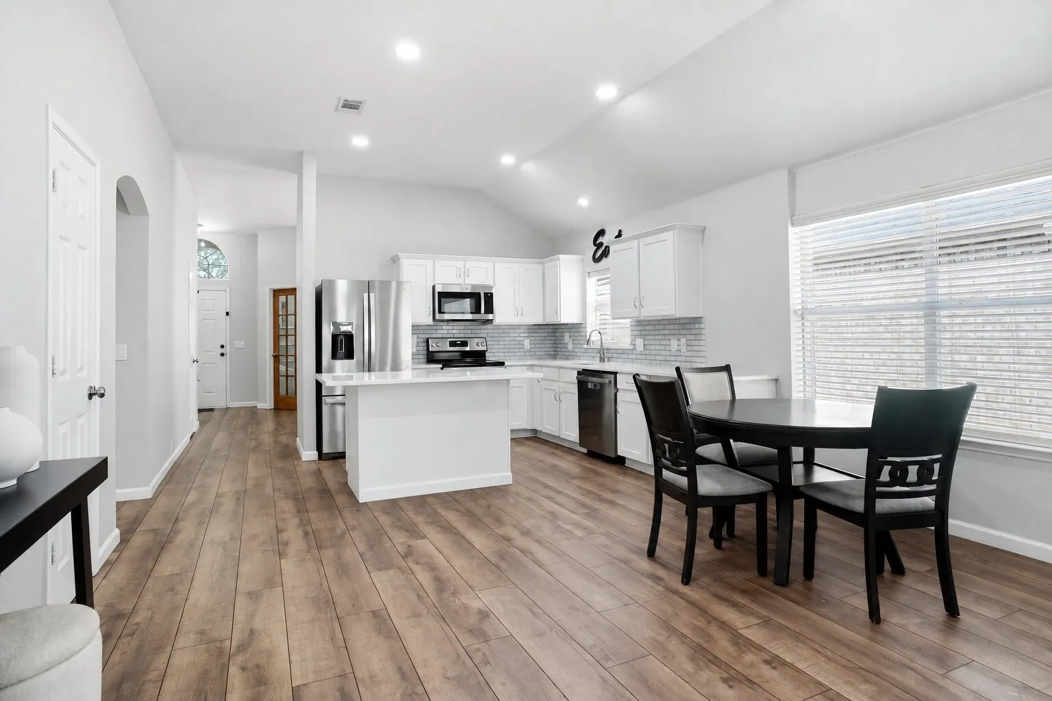 Bright, open kitchen and dining area featuring vaulted ceilings, abundant natural light, generous cabinet and counter space, and continuous wood-look flooring. Photos have been AI enhanced for presentation; no material property features were altered.