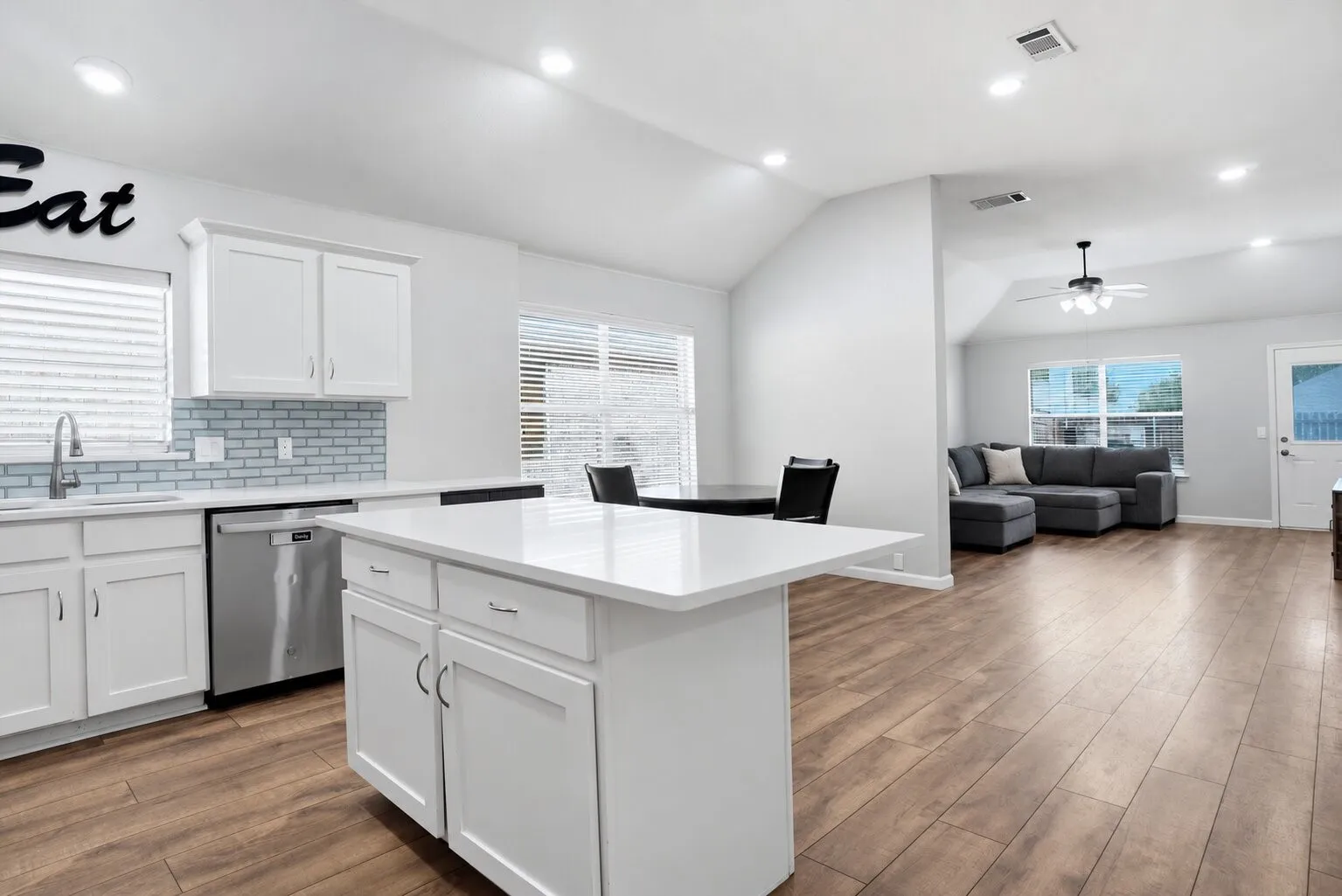 Open-concept kitchen and living area featuring a large quartz island, stainless steel appliances, abundant natural light, and durable wood-look flooring throughout. Photos have been AI enhanced for presentation; no material property features were altered.