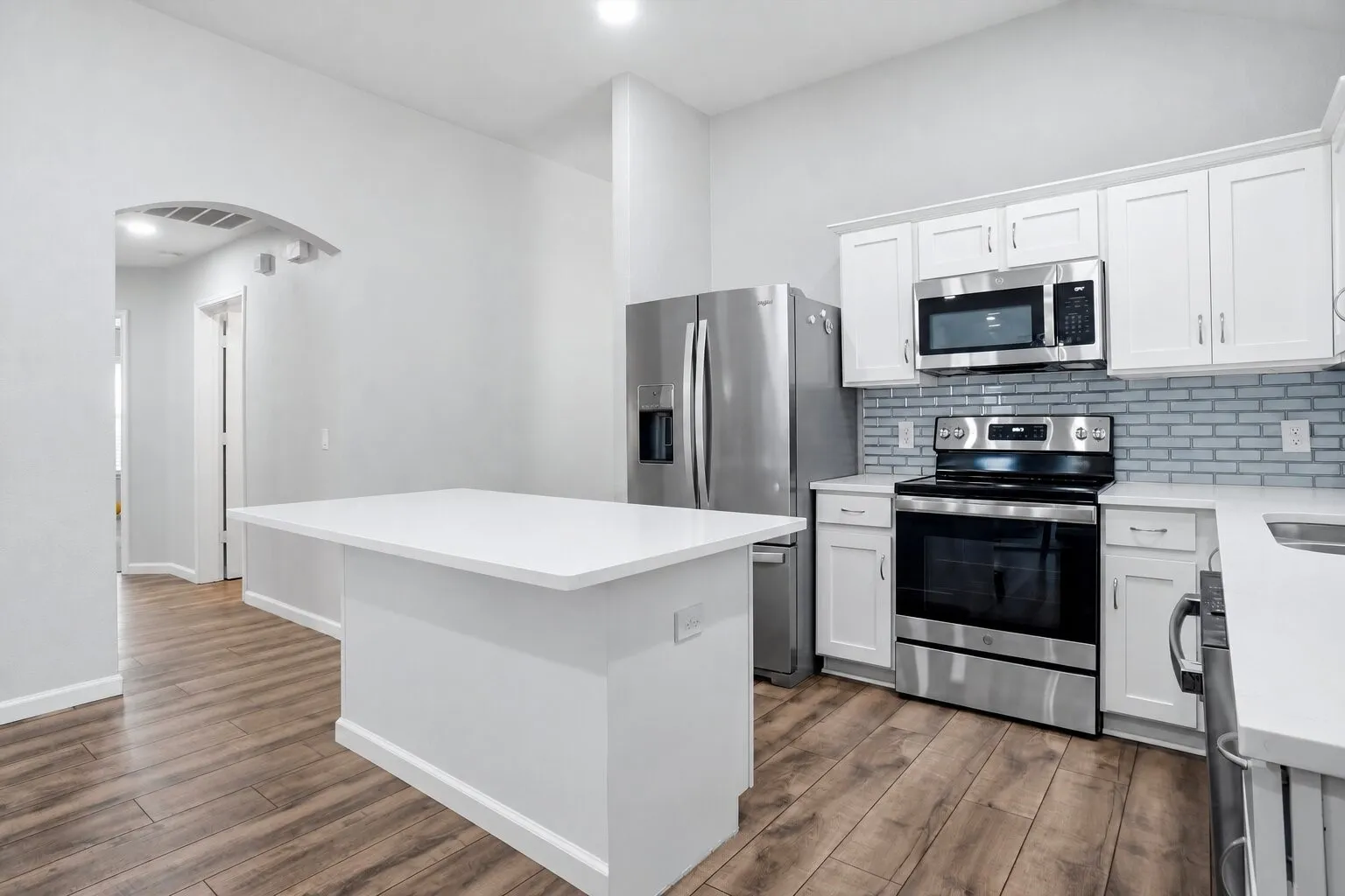 Updated kitchen with an oversized quartz island, white shaker-style cabinetry, subway tile backsplash, stainless steel appliances, and wood-look flooring. Photos have been AI enhanced for presentation; no material property features were altered.