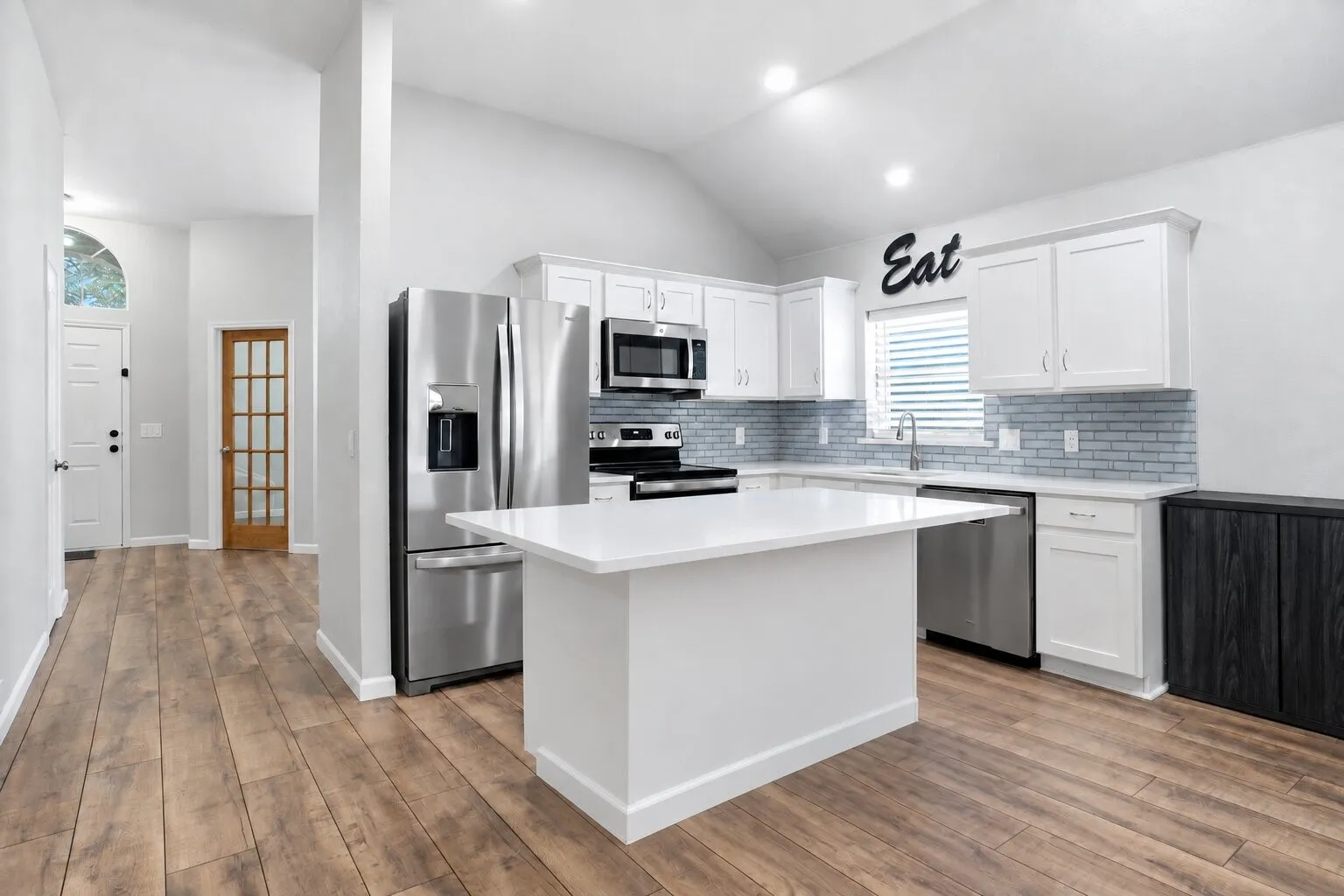 Bright, updated kitchen featuring an oversized quartz island, white shaker-style cabinetry, subway tile backsplash, stainless steel appliances, and recessed lighting. Photos have been AI enhanced for presentation; no material property features were altered.