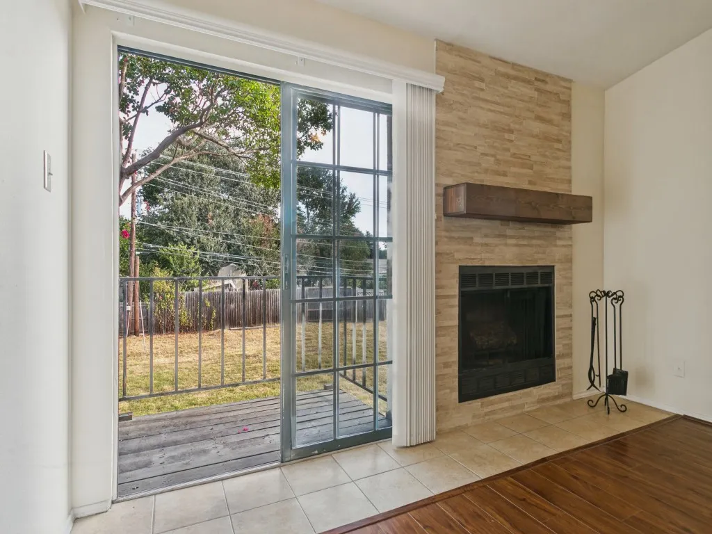 Sliding glass door, stone-finish fireplace, wood mantel, tile flooring, and wood-finish flooring