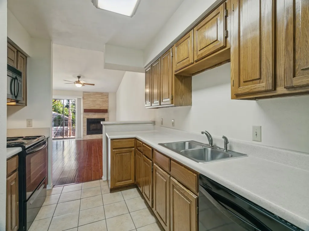 Kitchen featuring light wood-finish cabinetry, white countertops, a double basin stainless steel sink, black built-in appliances, and tile flooring