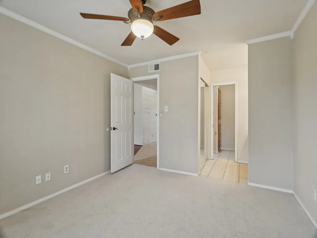 Neutral-toned walls with crown molding, carpeted flooring, and a ceiling fan with integrated lighting