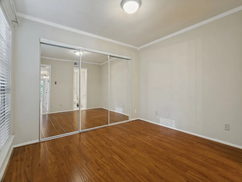 Wood-finish flooring, white walls, crown molding, ceiling-mounted light fixture, and mirrored closet doors
