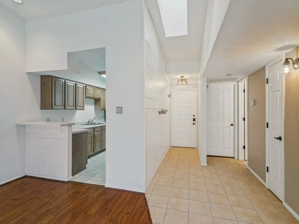 Kitchen pass-through with breakfast bar, wood-finish flooring, tile flooring, white paneled doors, and a skylight