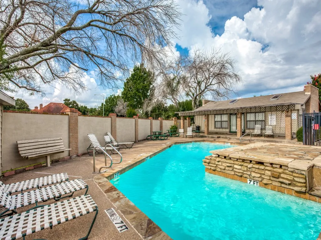 Swimming pool with stone coping, a stone-faced raised spa, extensive concrete decking, and perimeter privacy fencing